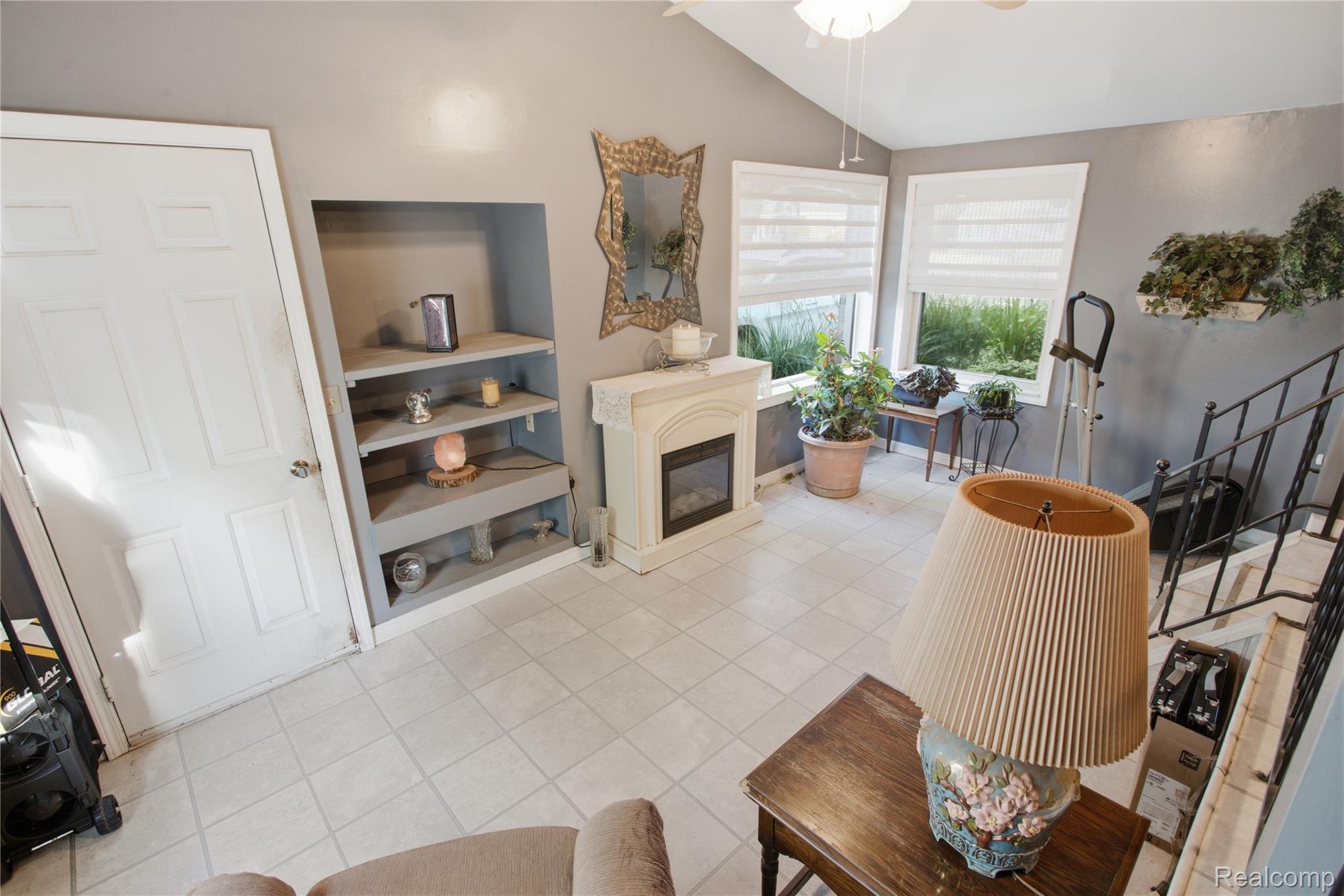 Sitting area with built-in shelves, a fireplace, tiled floor, and staircase.