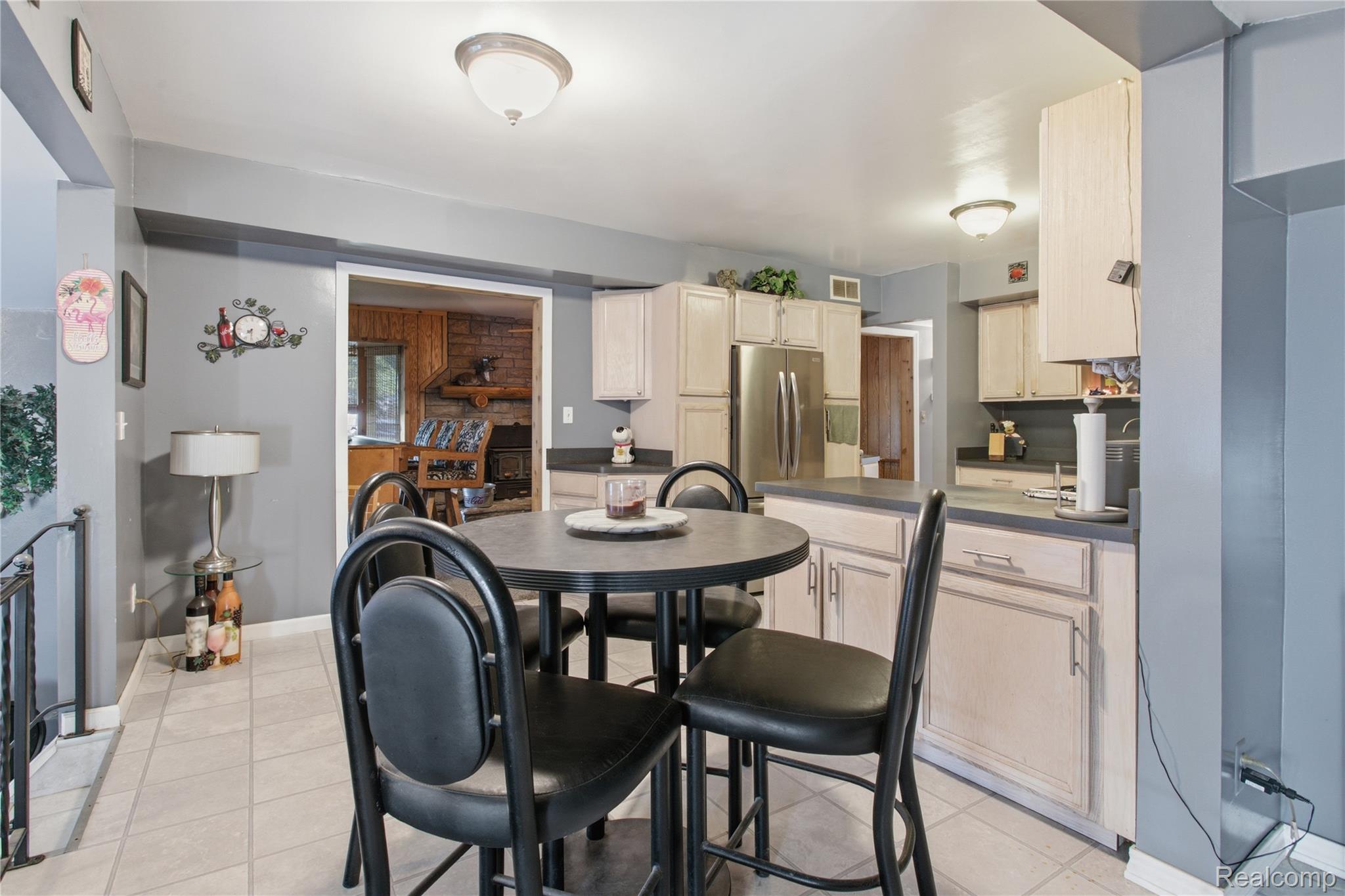 Kitchen and dining area with light cabinets, stainless refrigerator, and round table with black chairs.