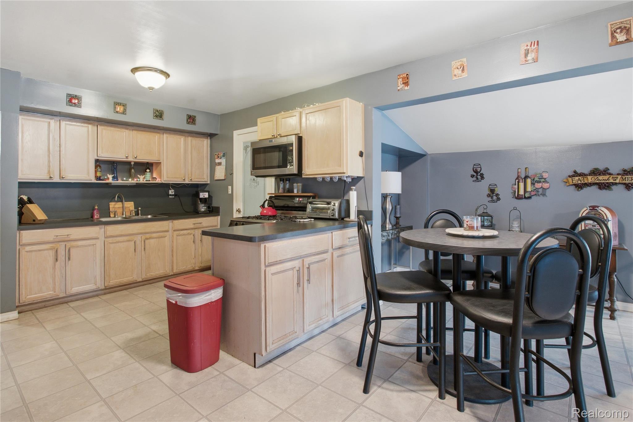 Kitchen with light wood cabinets and island beside a round dining table with black chairs.