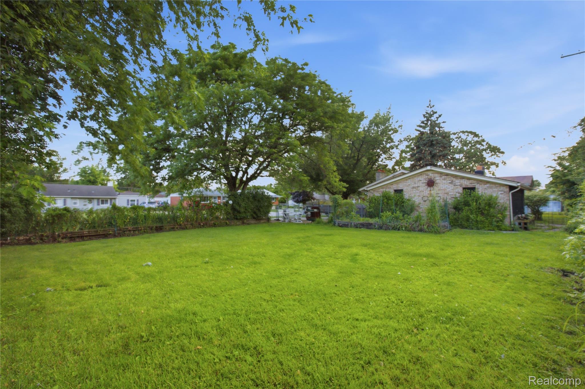 Broad green backyard with mature trees, hedges, and a brick house along the right side.