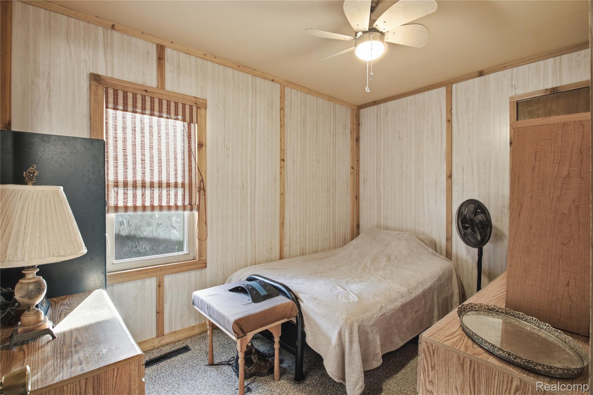 Small bedroom with a bed, wood-trimmed paneled walls, and a window with a woven shade.
