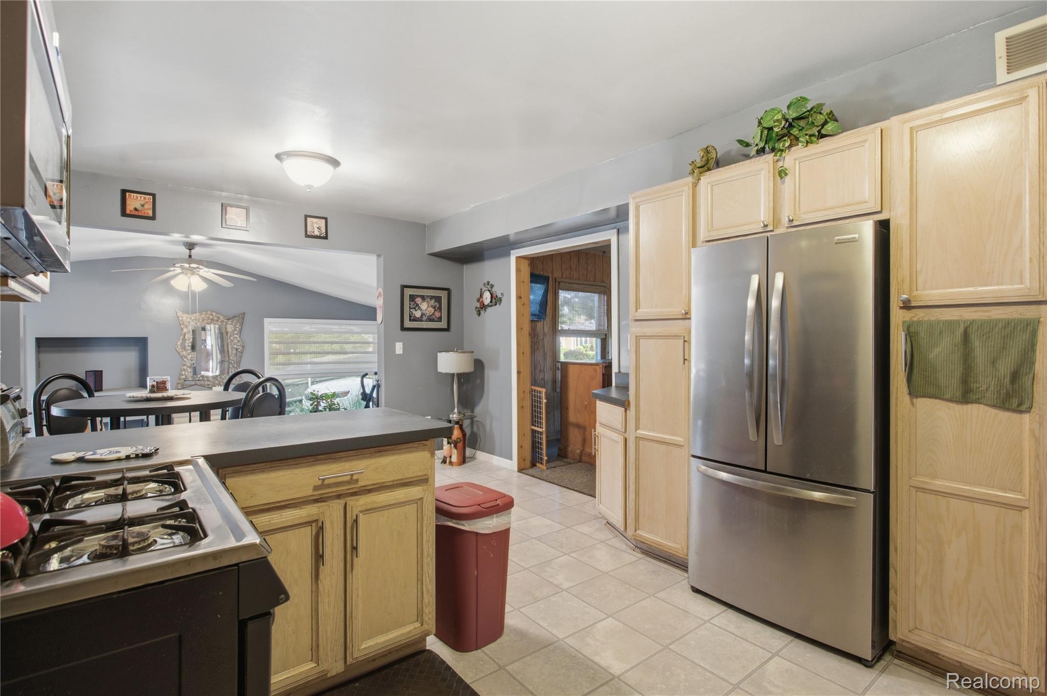 Kitchen with light wood cabinets, stainless steel refrigerator, tiled floor, and central island.