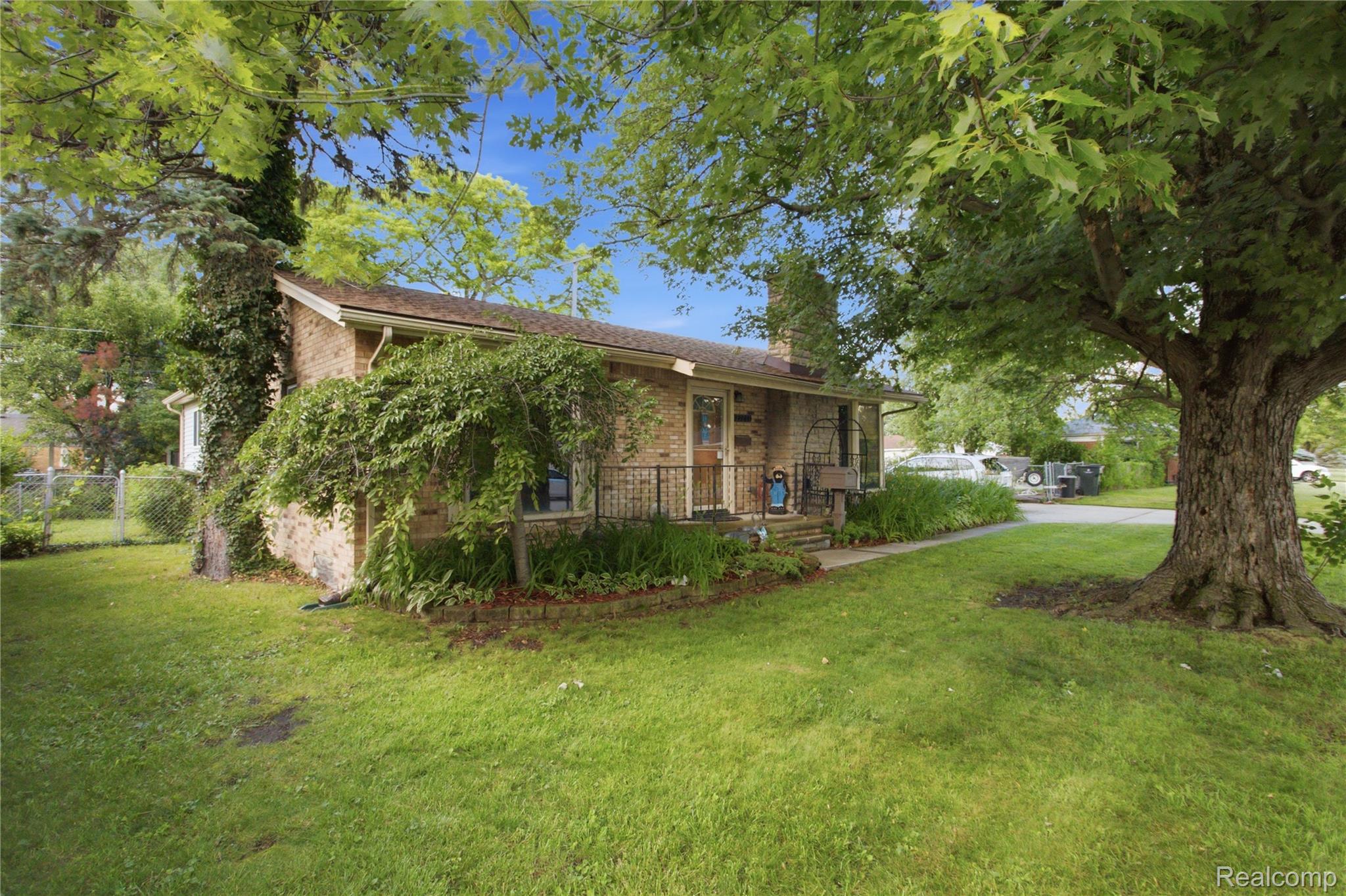 Brick ranch home with a covered porch, leafy landscaping, and a large shade tree in the front yard.