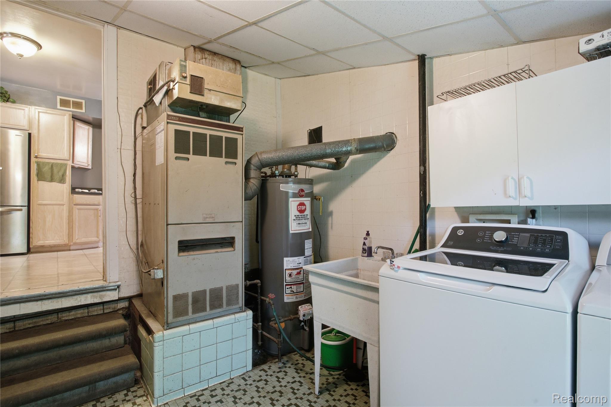 Basement laundry and utility area with a furnace, hot water tank, utility sink, and washing machine.