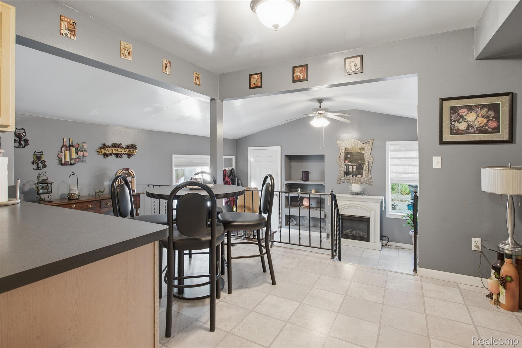 Dining area with a round table and black chairs beside a tiled living room with a fireplace.