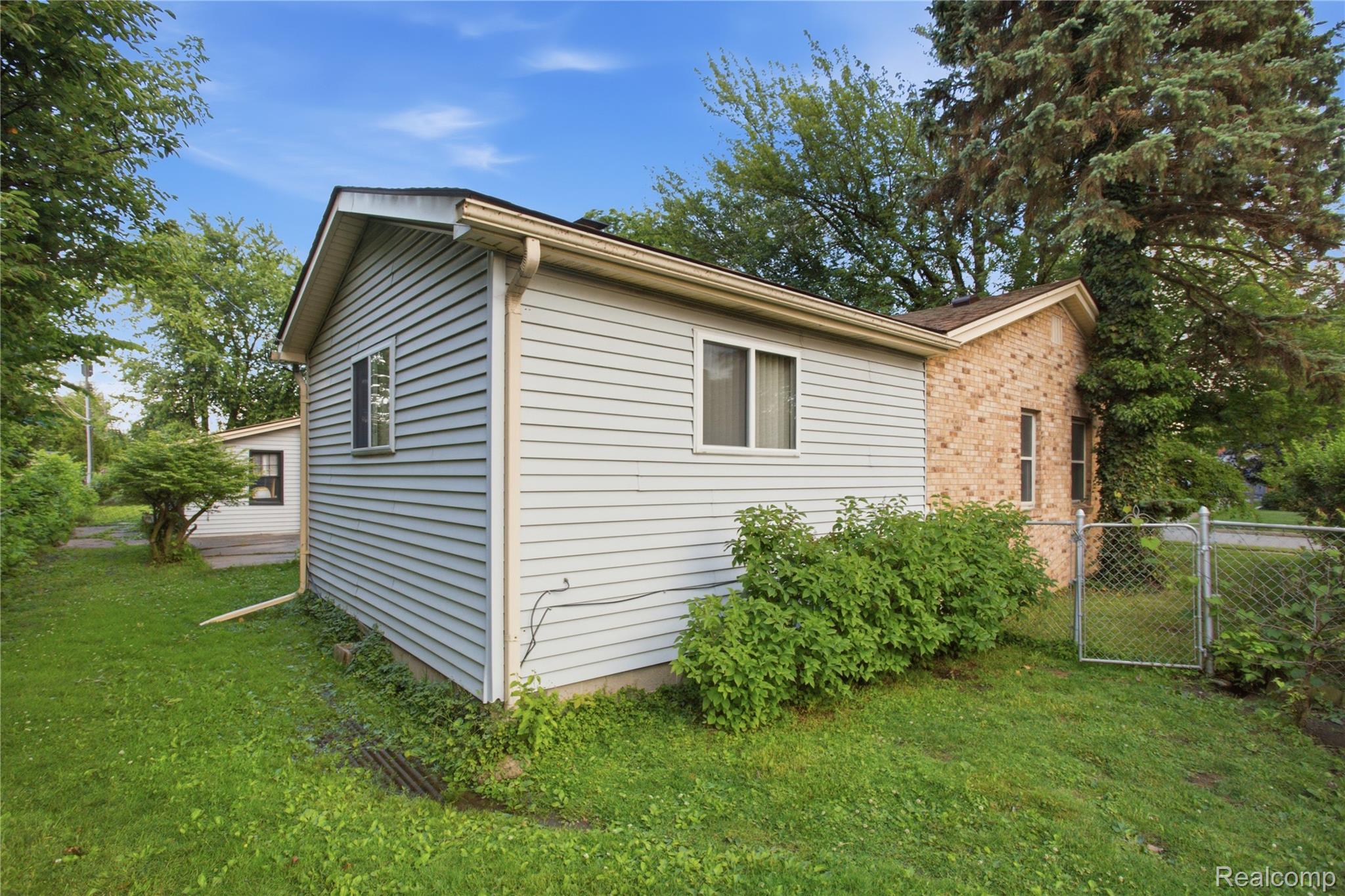 Side and rear of a house with white siding, a brick section, and a fenced grassy yard.