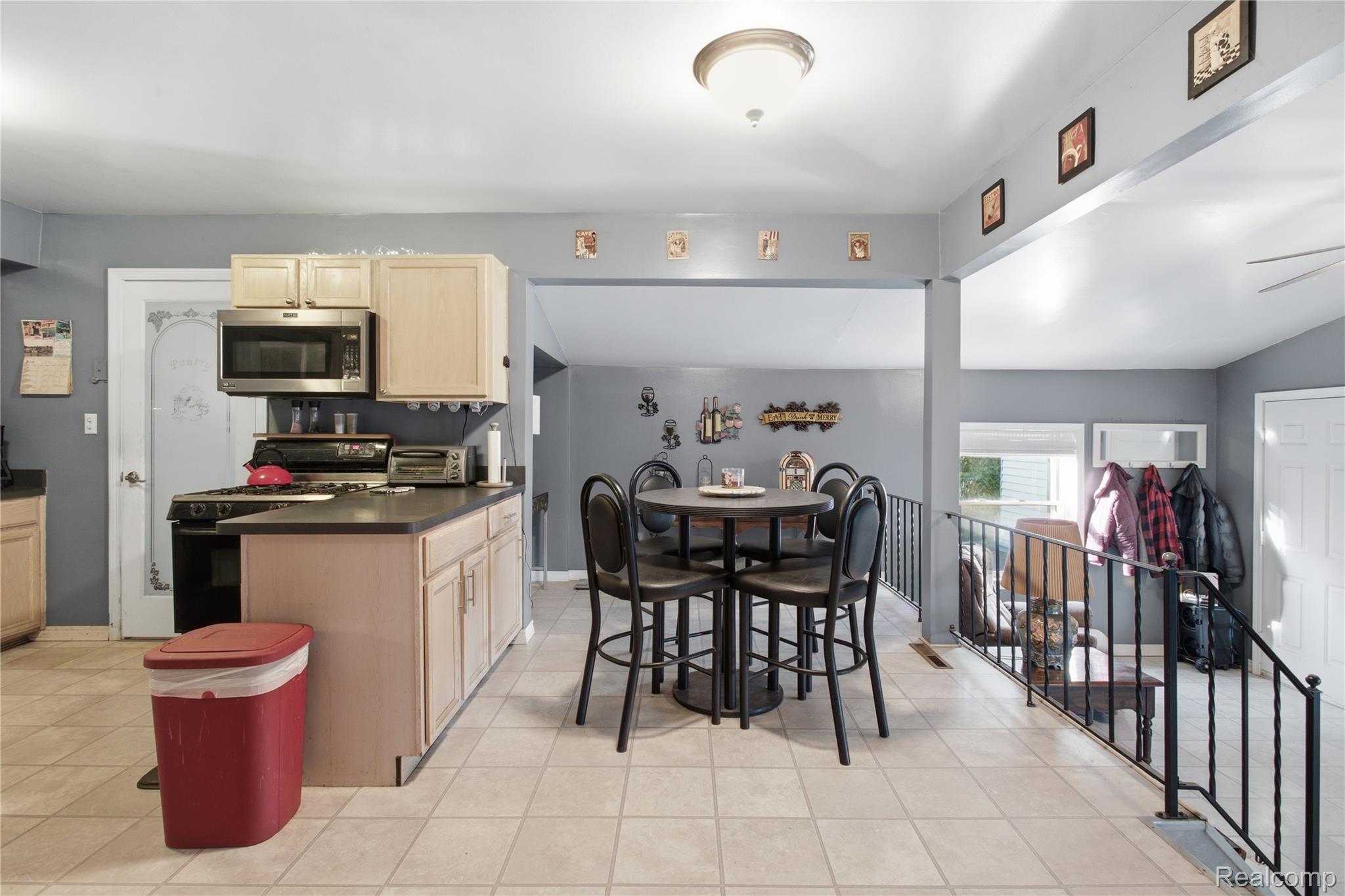 Kitchen and dining area with light wood cabinets, a round table, and railing beside the stair opening.