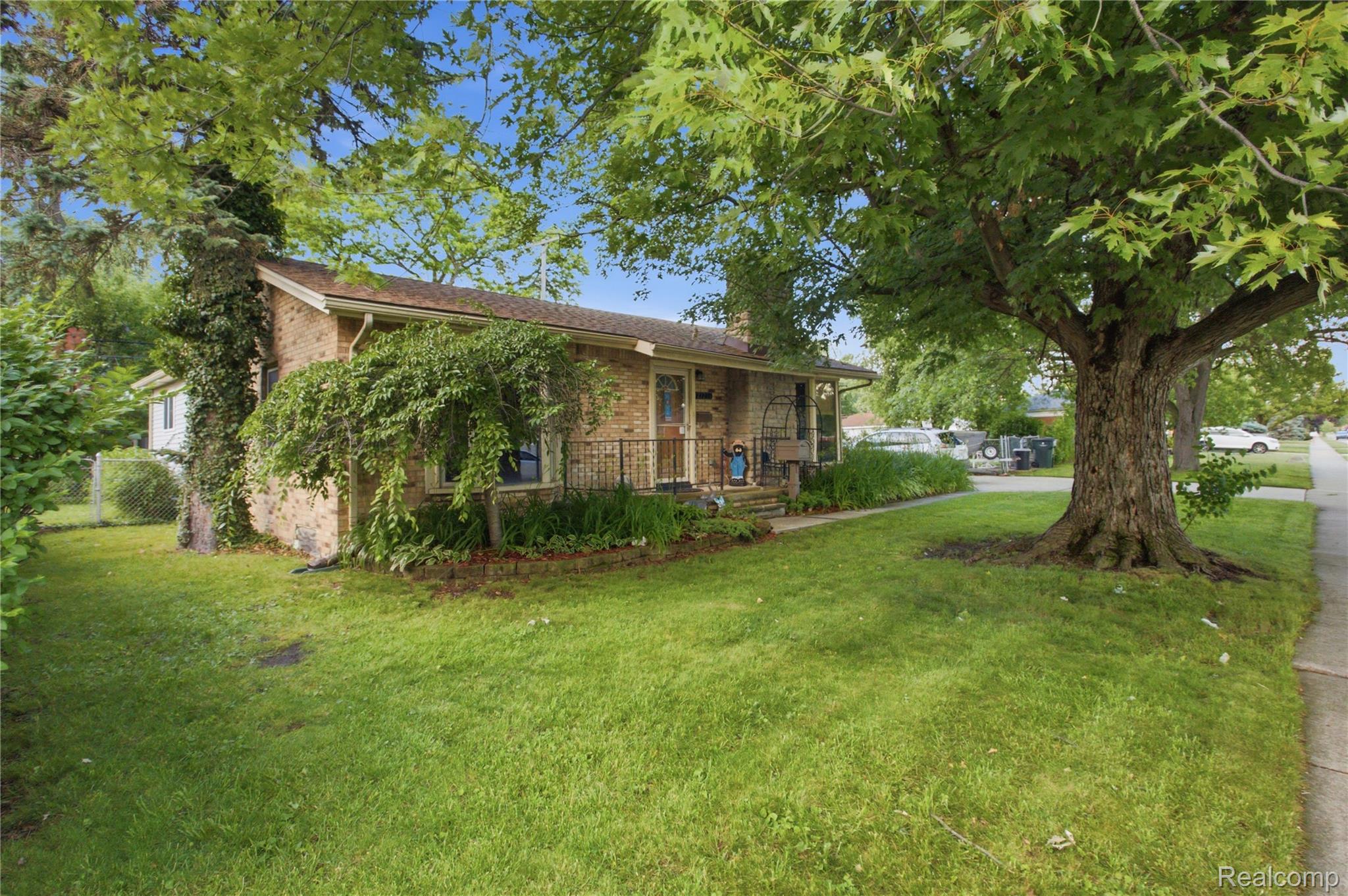 Brick ranch home with a covered porch, landscaped yard, and large shade tree.