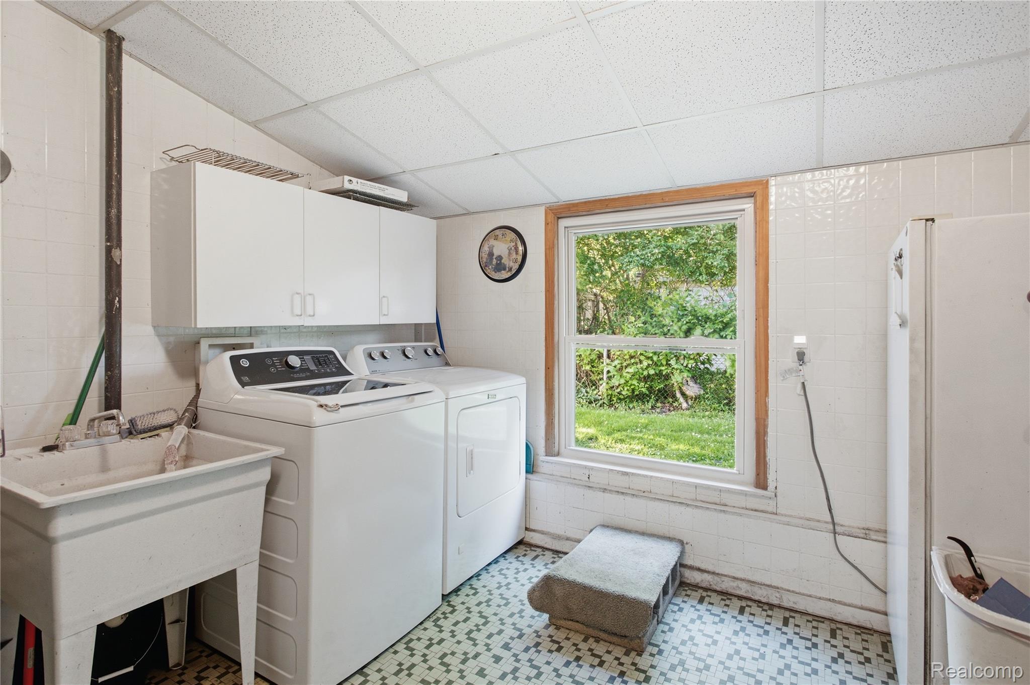 Laundry room with washer, dryer, utility sink, and a window overlooking greenery.