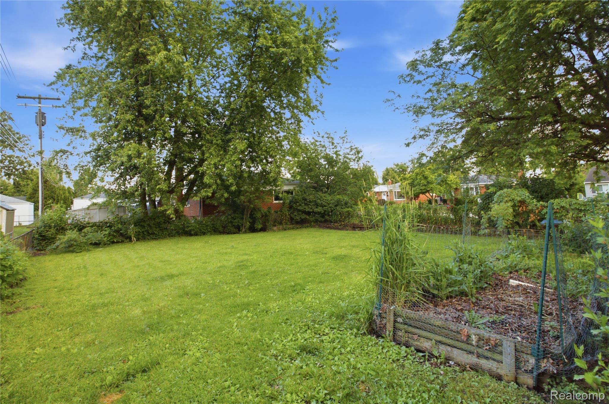 Backyard lawn shaded by mature trees, with a fenced raised vegetable garden.