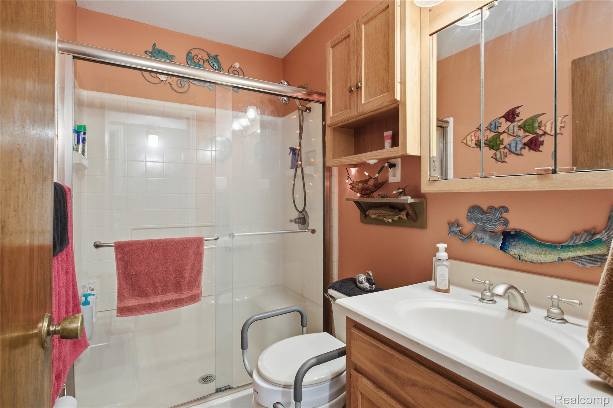 Bathroom with a glass shower, wood vanity, coral walls, and decorative fish.