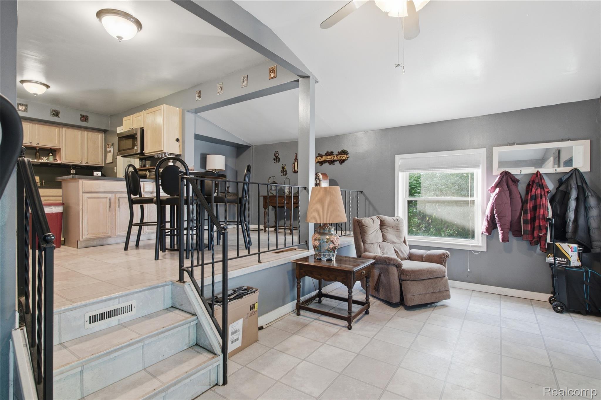 Living area with recliner beside a window, overlooking a raised kitchen and dining space.