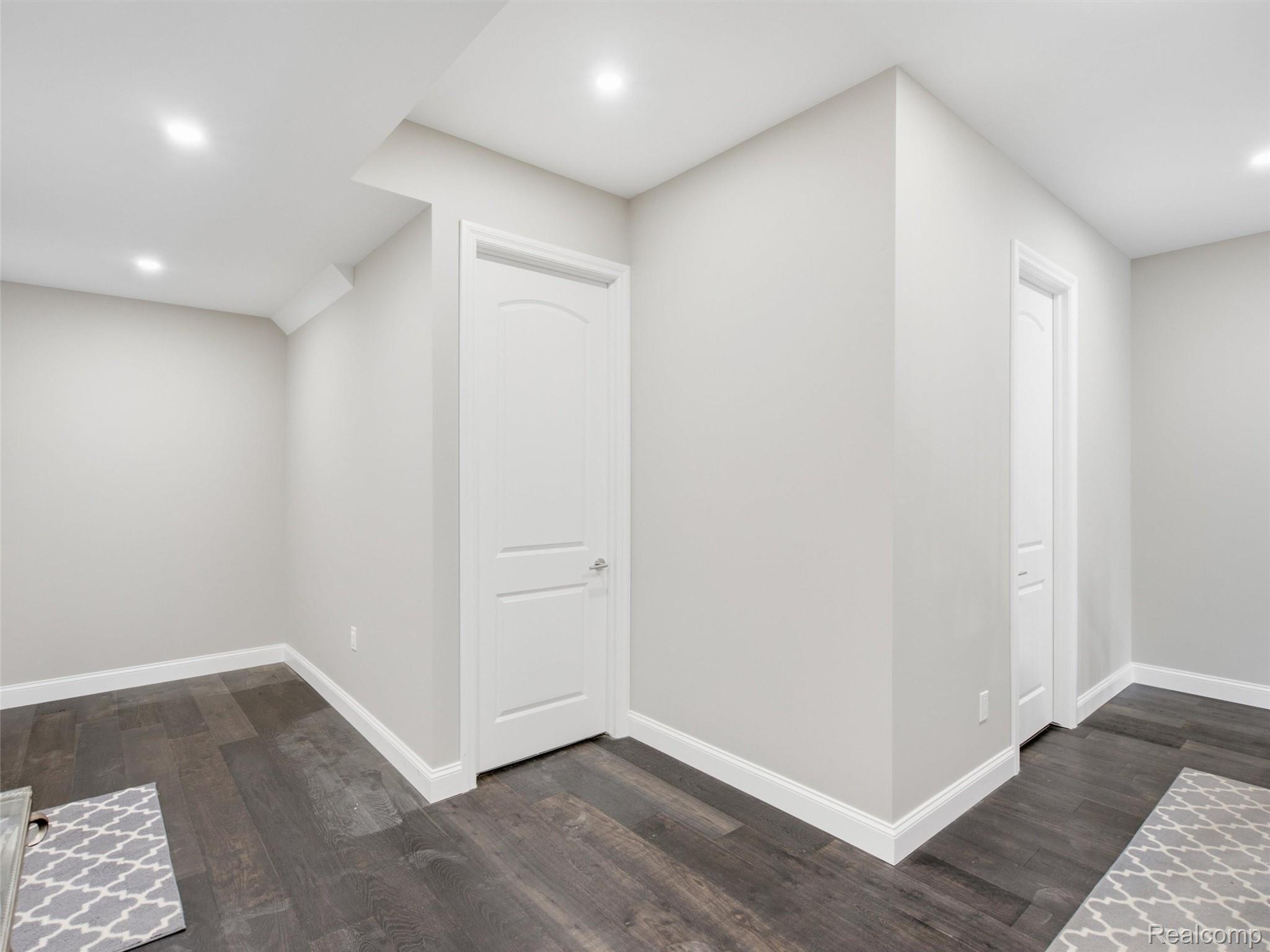 Empty hallway with two white paneled doors, angled ceilings, and dark flooring.