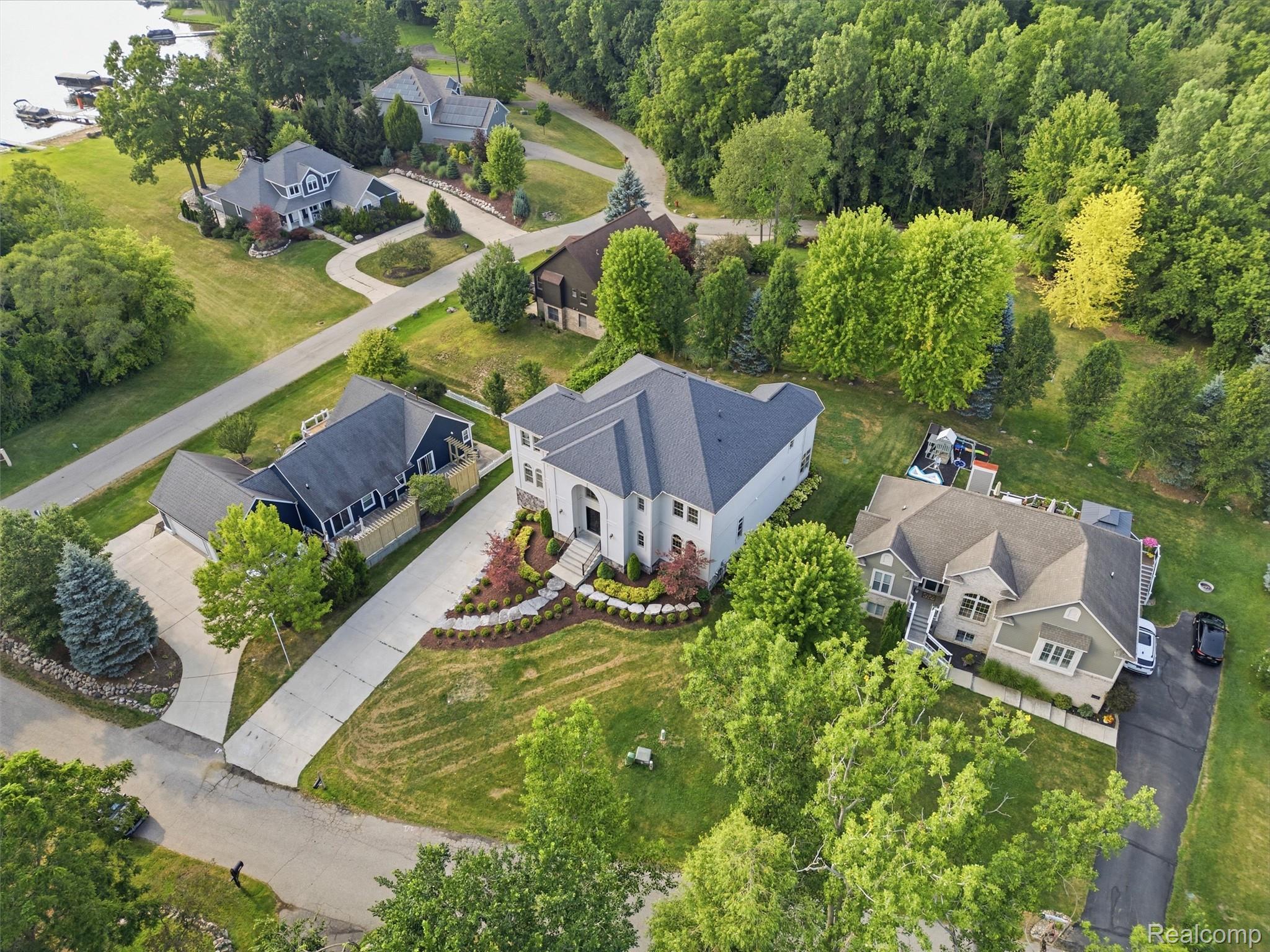 White two-story home with a gray roof, landscaped garden, and driveway, seen from above.