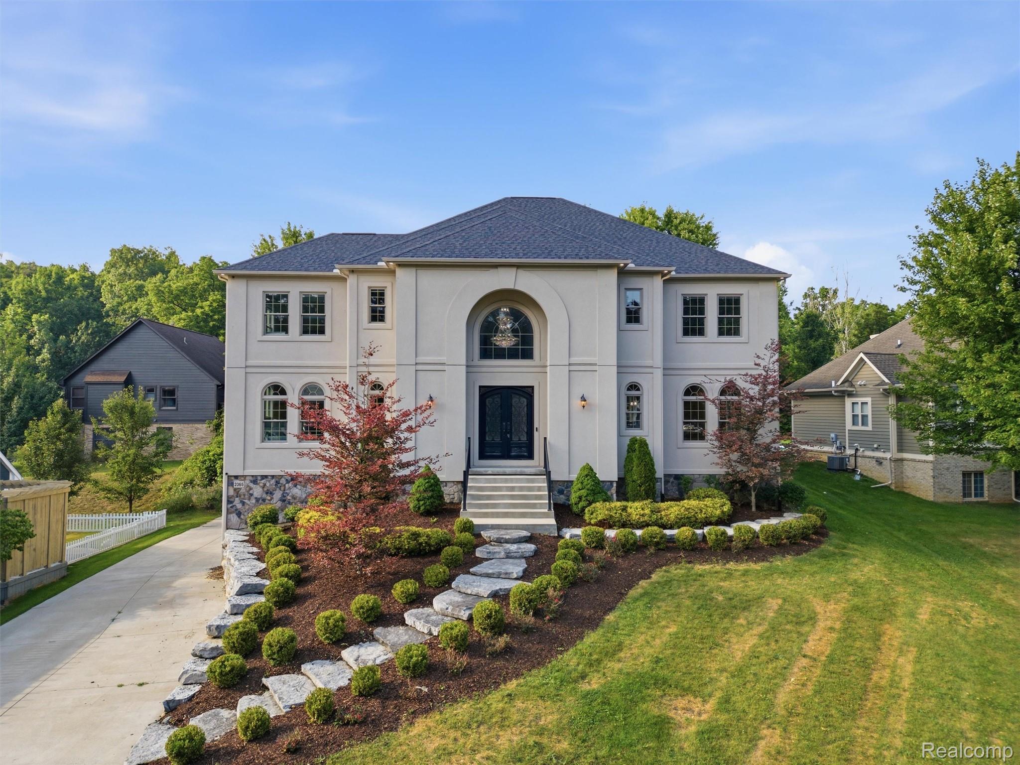 Two-story home with an arched entry, stone accents, landscaped front garden, and broad lawn.
