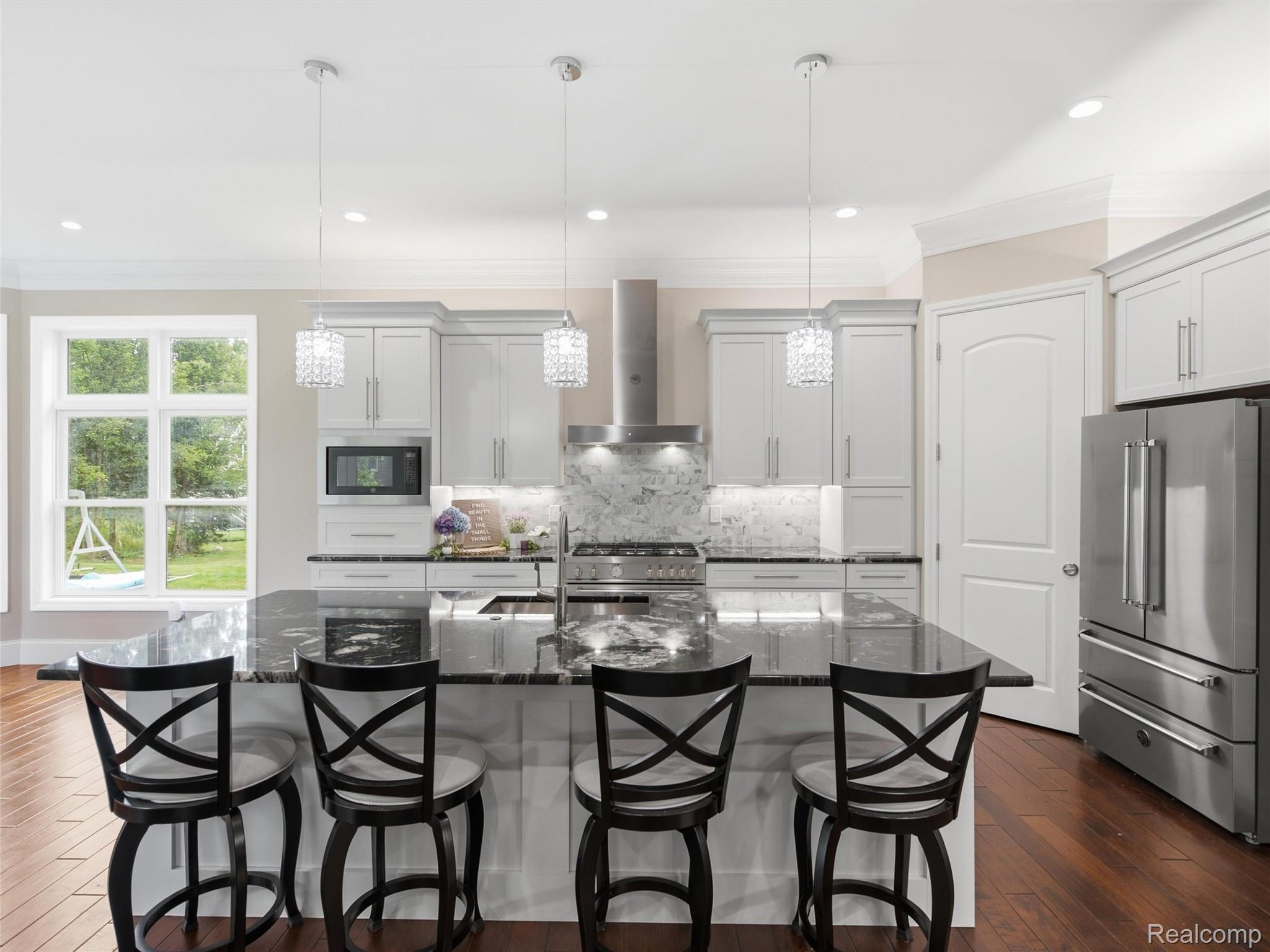 Bright kitchen with a large dark stone island, four bar stools, white cabinets, and stainless steel appliances.