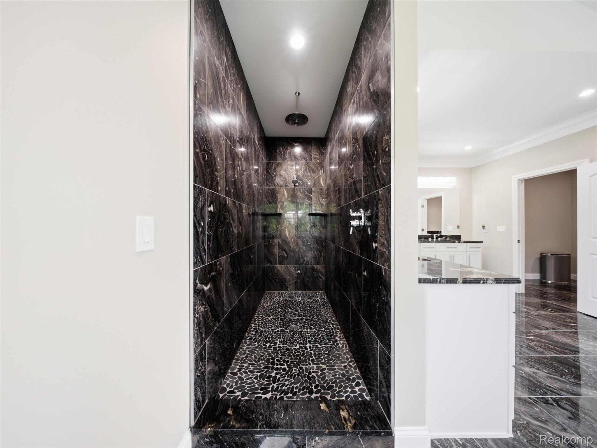 Walk-in shower with dark marble-look tile, a pebble-pattern floor, and a ceiling-mounted rainfall showerhead.
