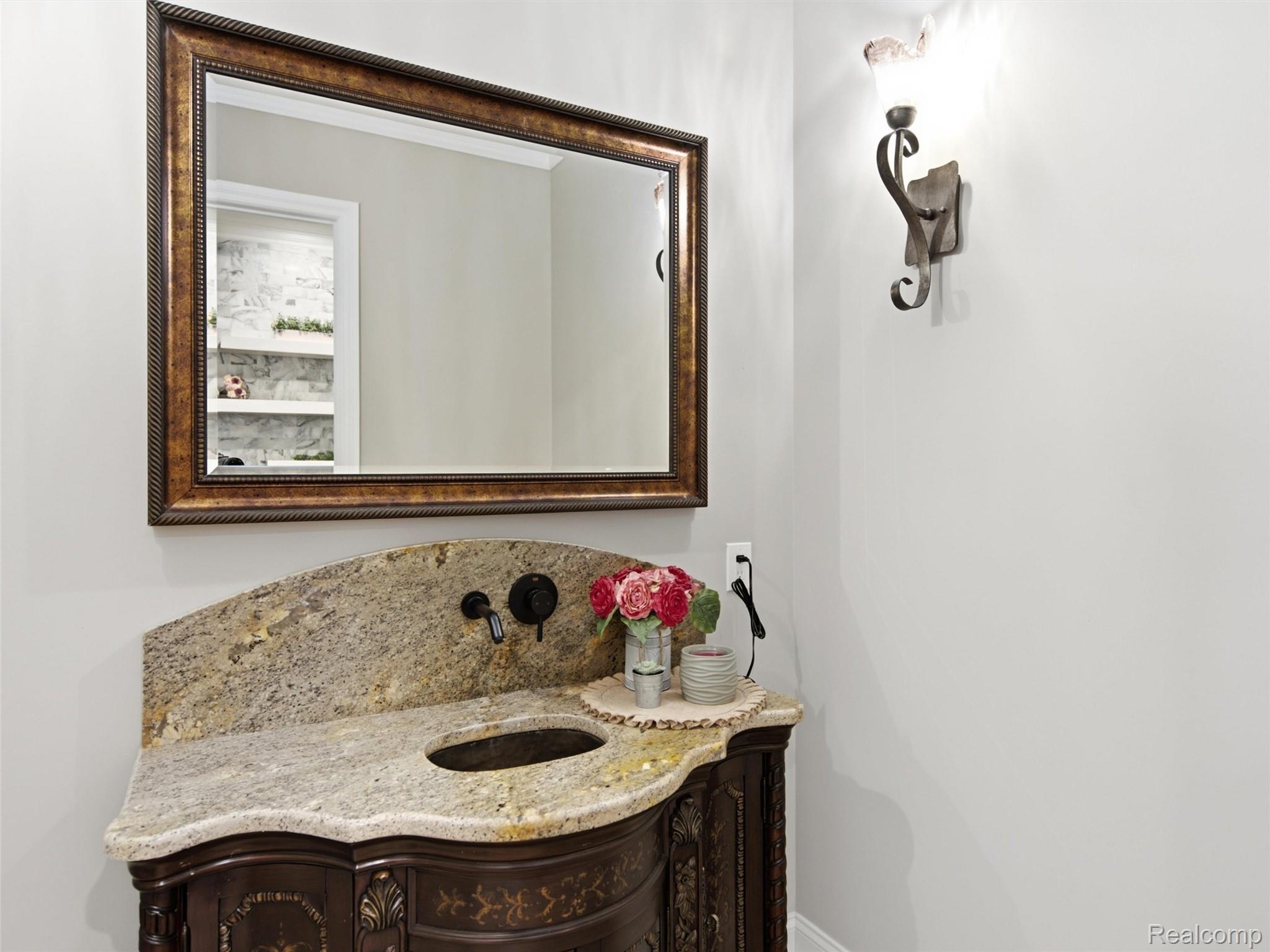 Bathroom vanity with a curved granite counter, ornate dark wood cabinet, and large framed mirror.