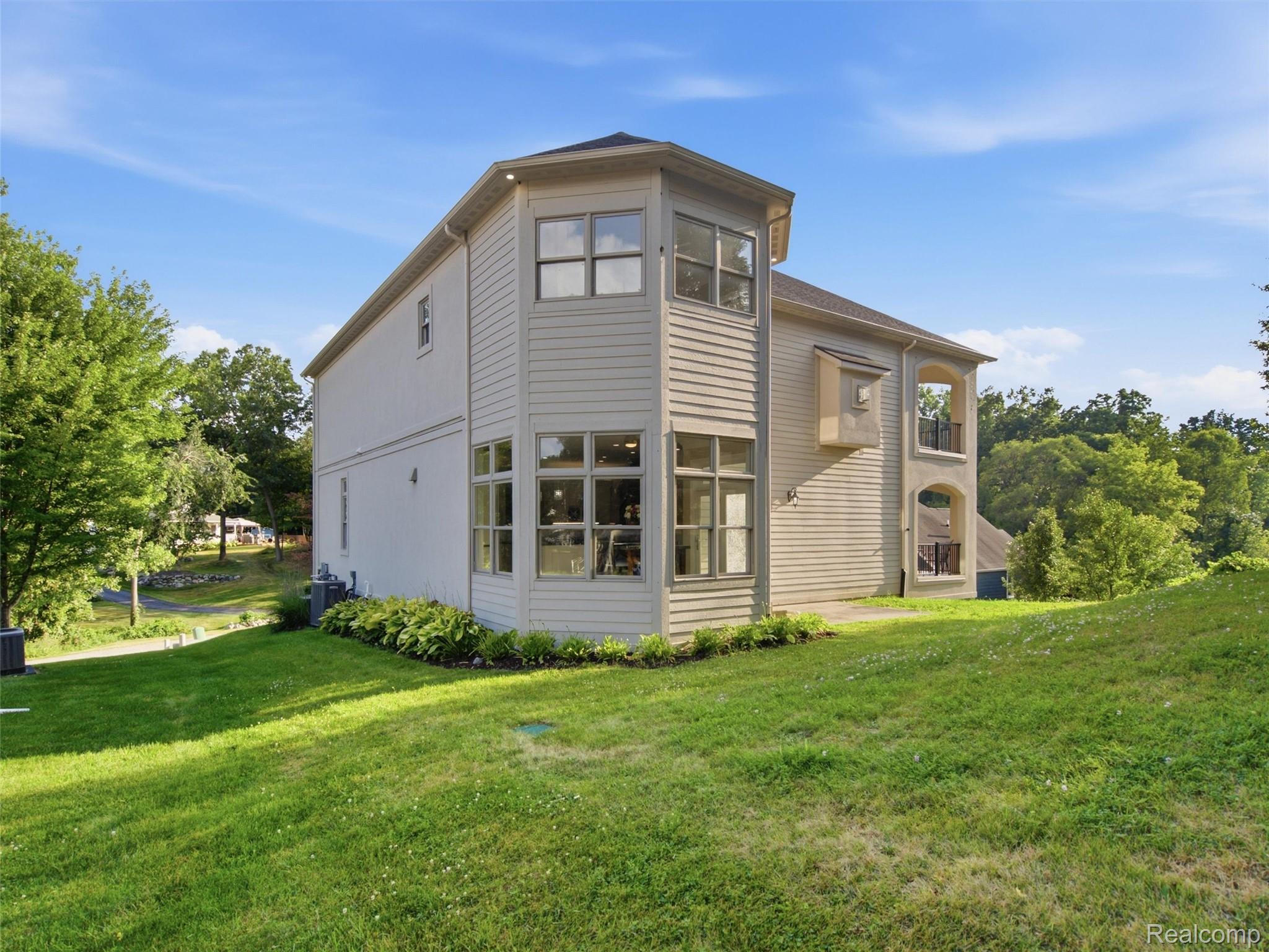 Two-story house with large windows and stacked balconies above a sloping lawn.