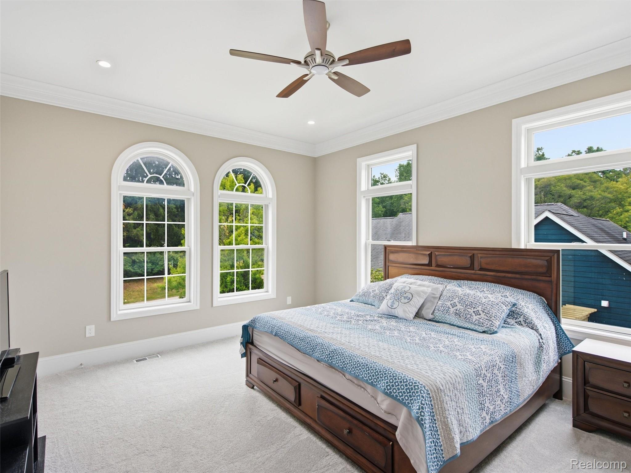 Bedroom with a dark wood bed, blue-and-white bedding, and arched windows overlooking trees.