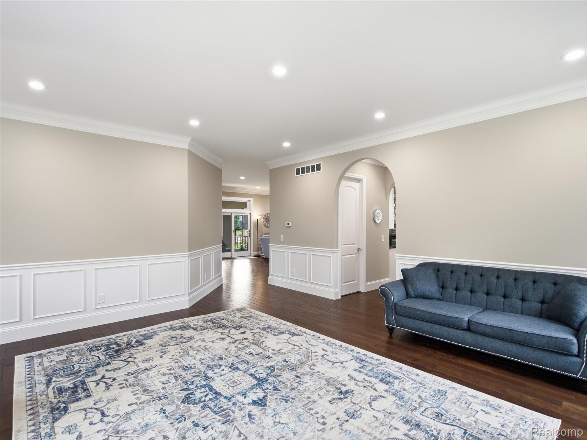 Living room with a blue tufted sofa, patterned rug, dark hardwood floors, and an arched doorway.
