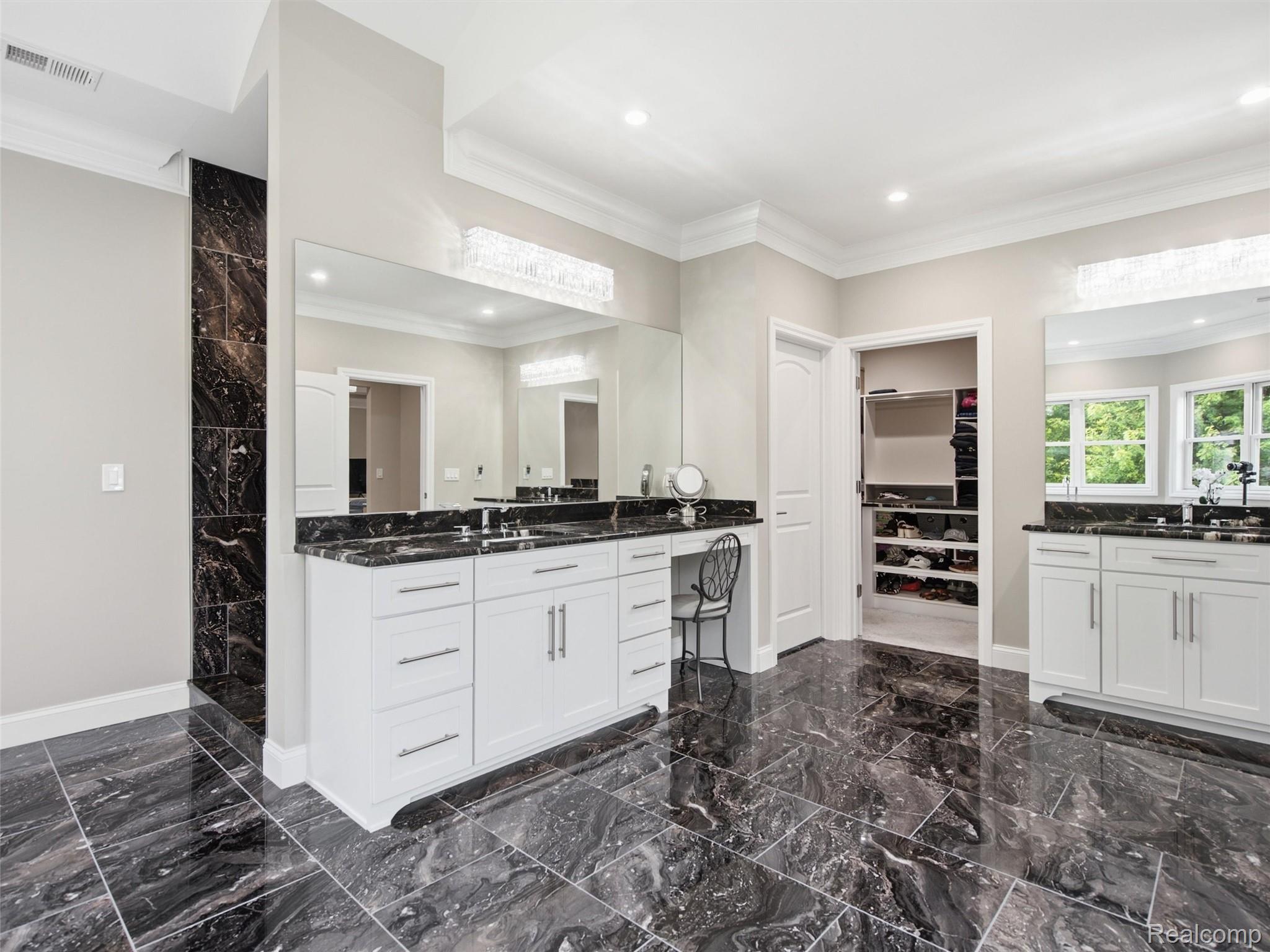 Bathroom with double white vanities, dramatic dark marble floors, and an open walk-in closet.