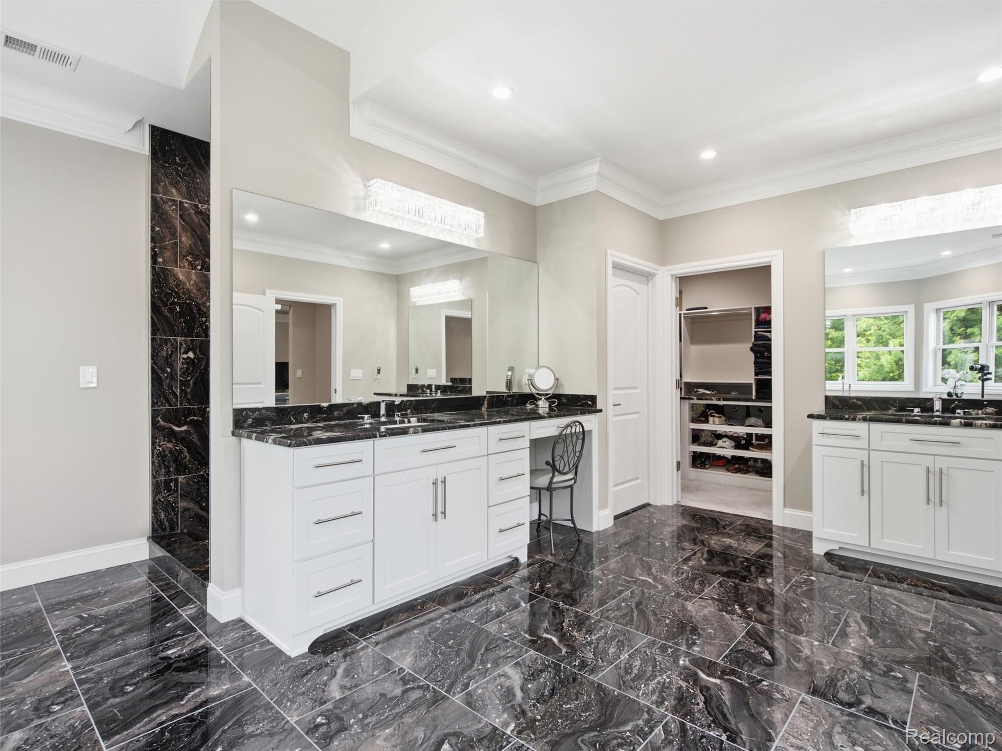 Bathroom with white vanities, dark marble surfaces, large mirrors, and an open walk-in closet.