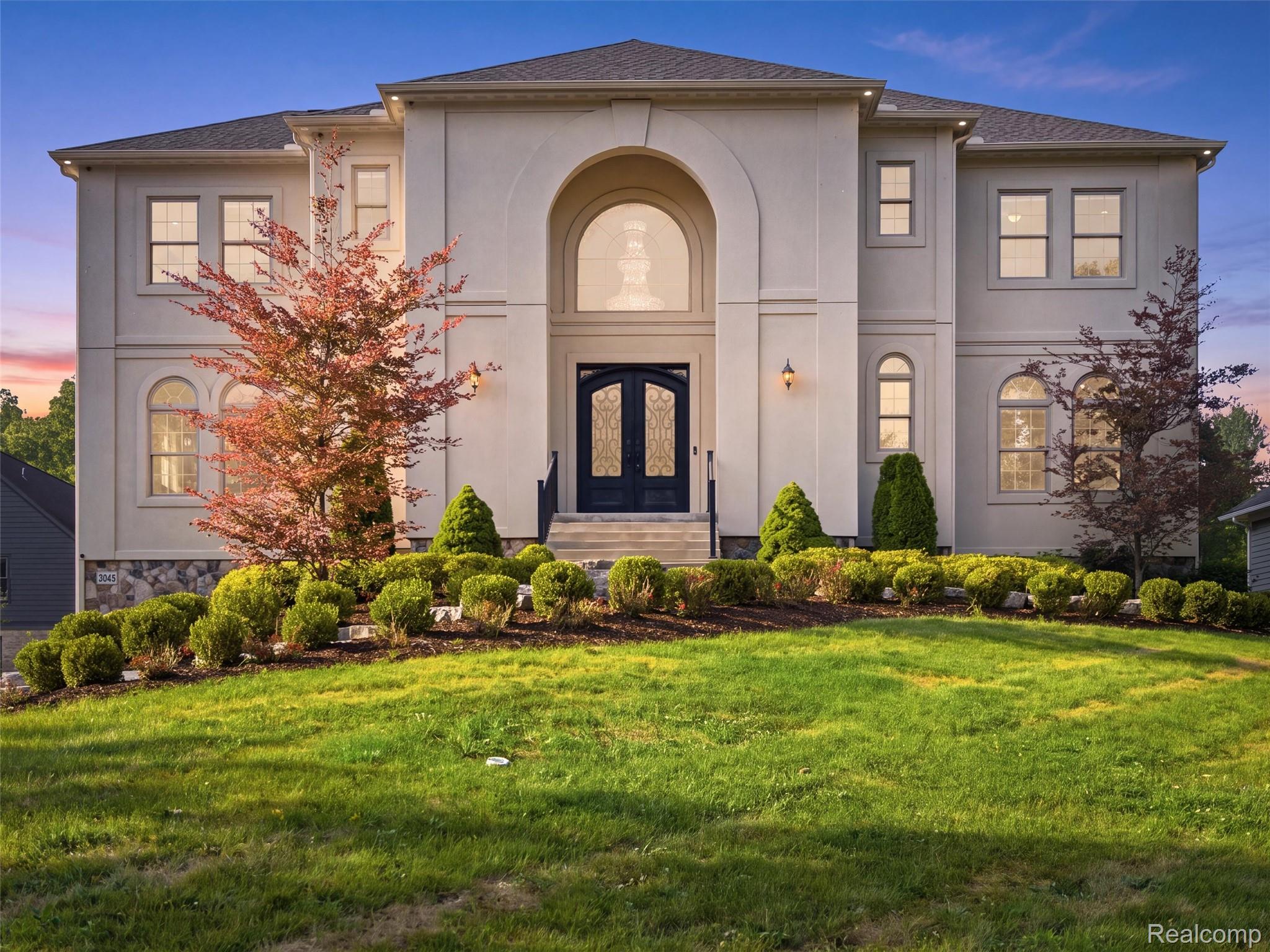 Two-story home with an arched entrance, dark double doors, and landscaped front lawn.