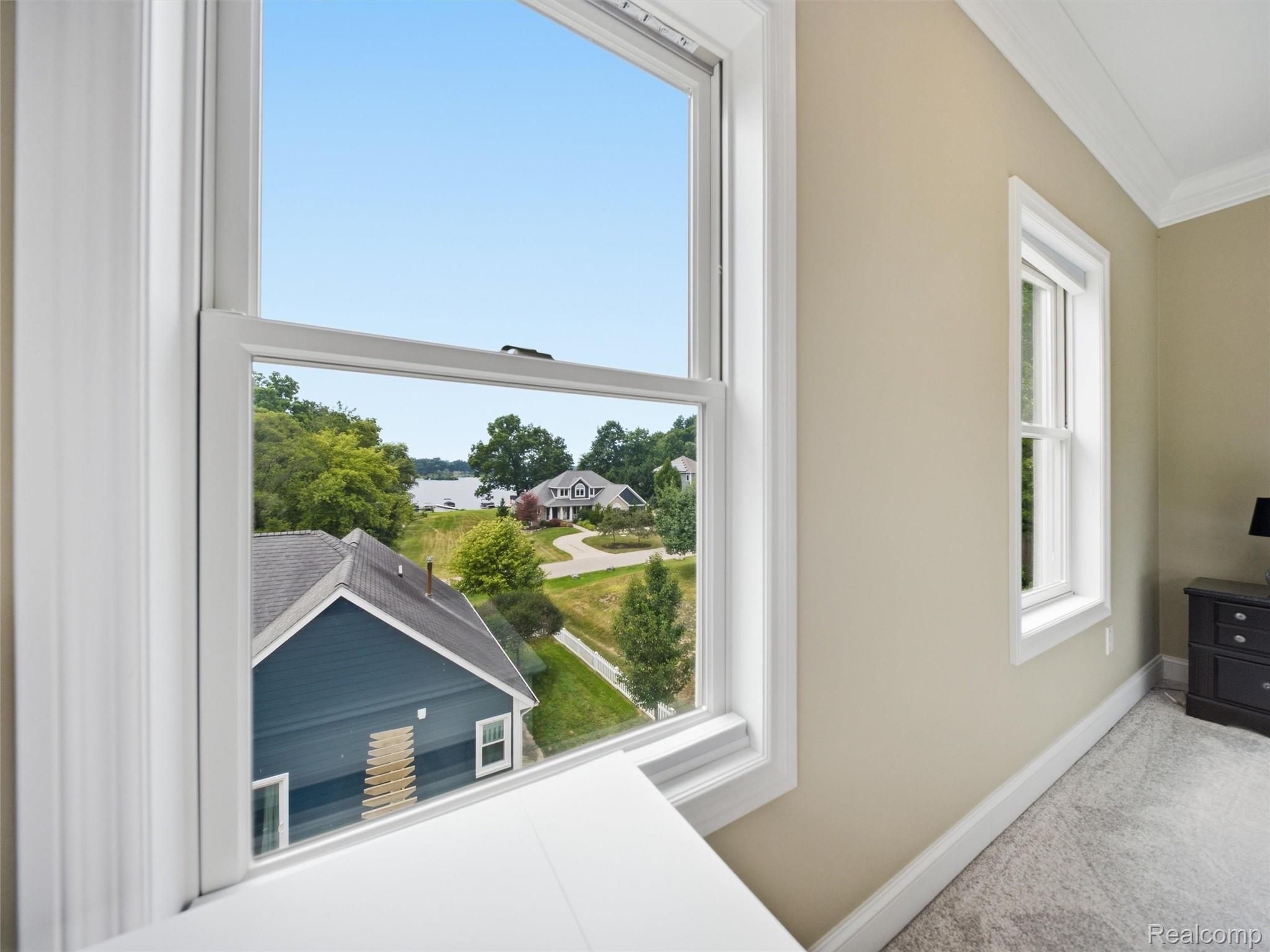 Room window overlooking a lake and neighboring homes, with a dark dresser and lamp nearby.