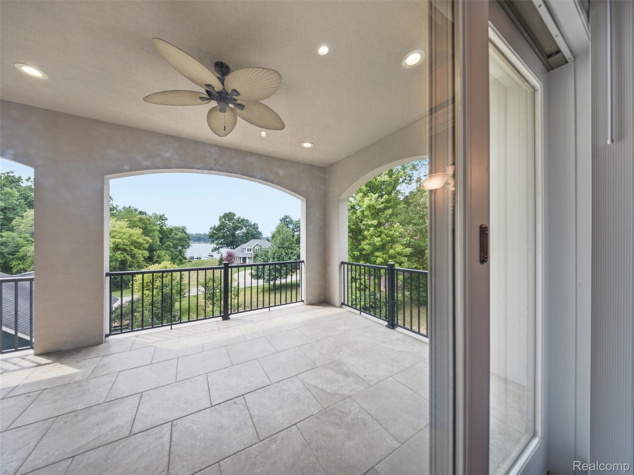 Covered tiled balcony with arched openings and a view of trees and a lake.
