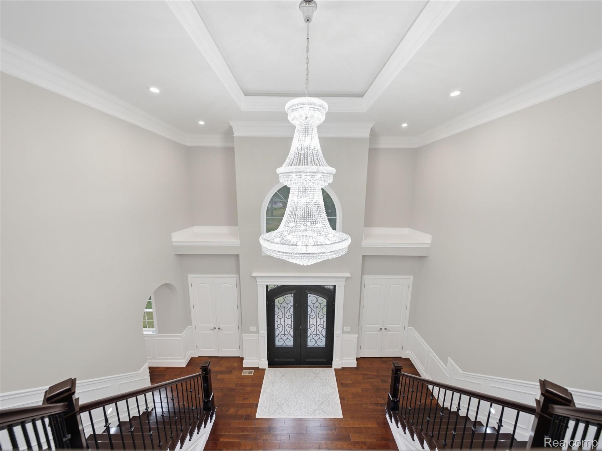 Two-story foyer with a crystal chandelier, dark wood floors, and decorative black entry doors.