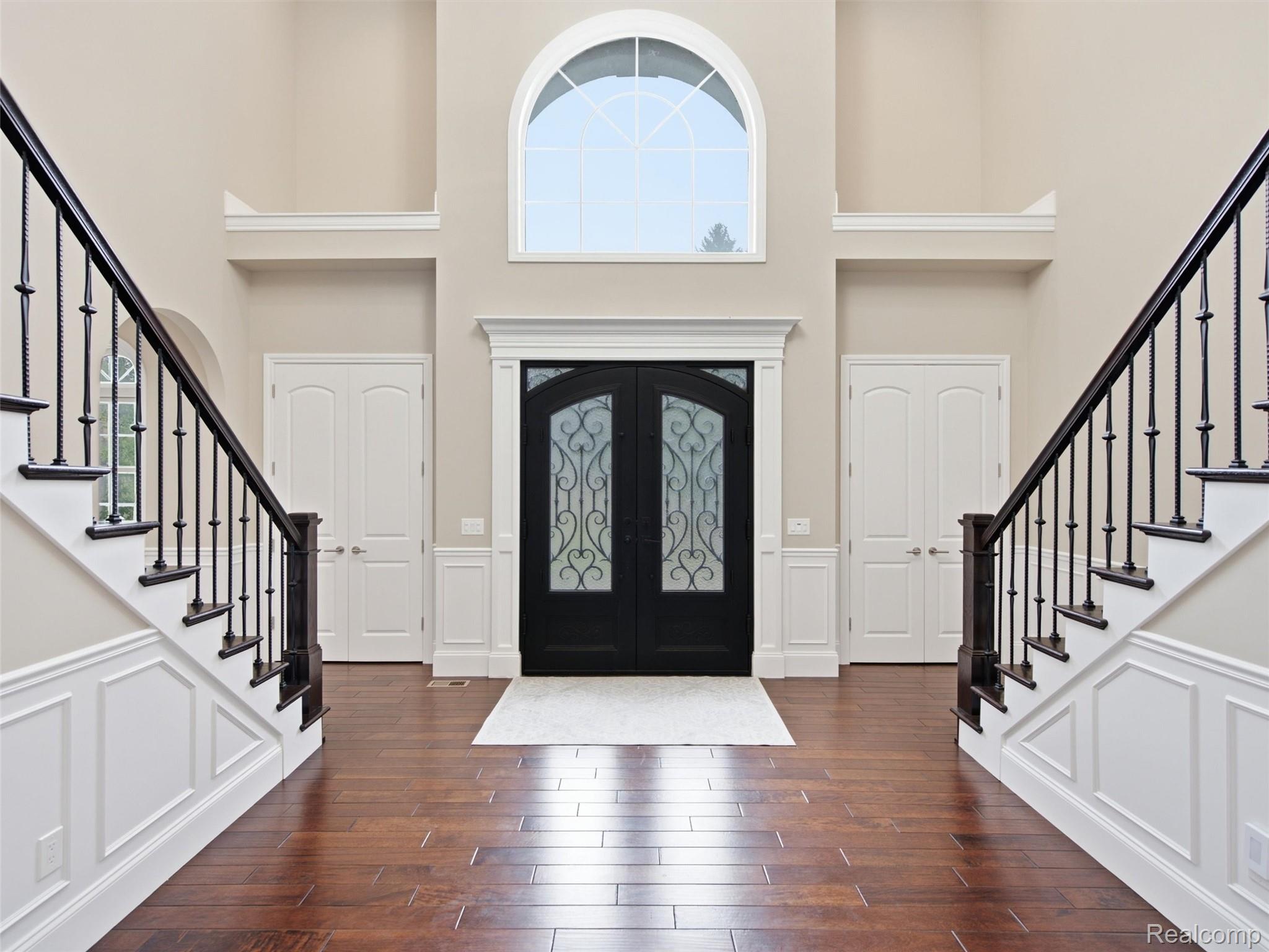 Two-story foyer with matching staircases, black decorative-glass doors, and an arched window.
