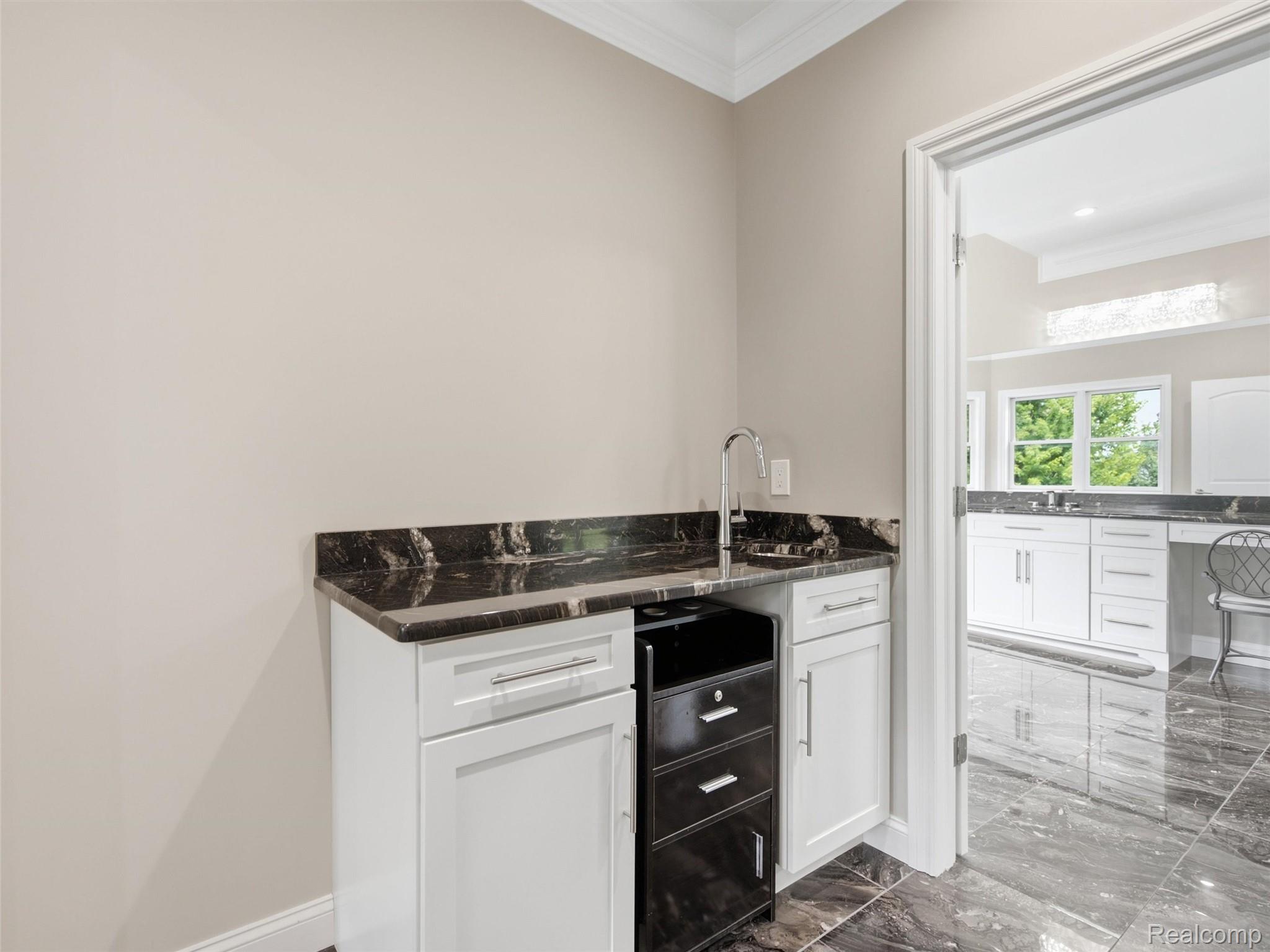 Built-in counter with dark stone surfaces, a sink, white cabinets, and an under-counter beverage refrigerator.