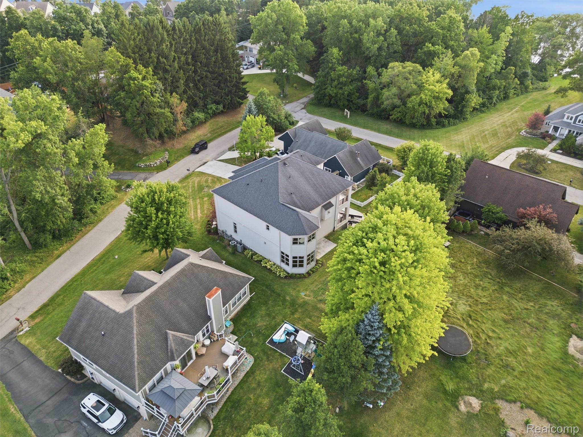 Aerial view of a white two-story home amid mature trees, neighboring houses, and a spacious lawn.
