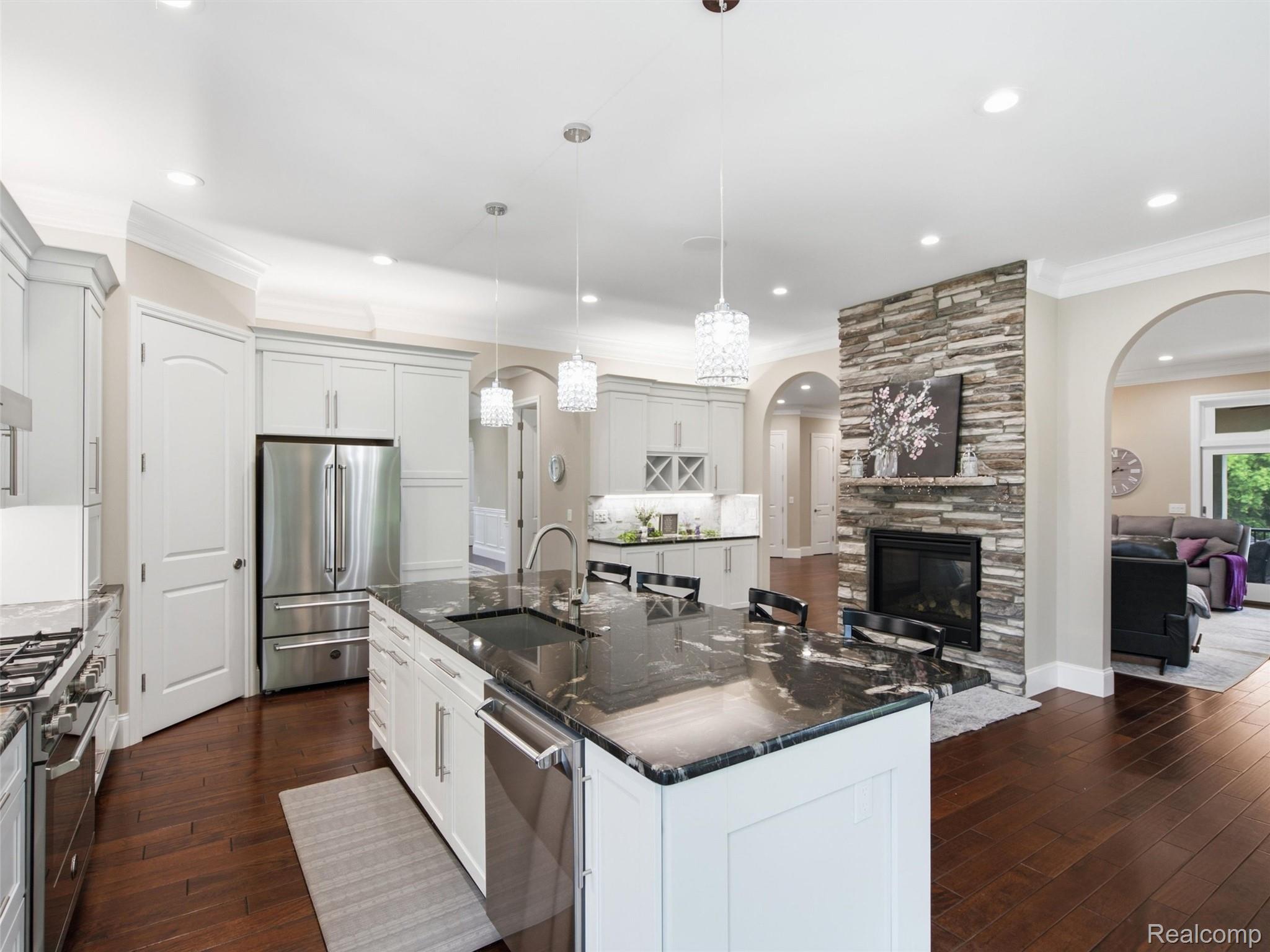 Kitchen with a large dark stone island, white cabinetry, stainless steel appliances, and a stone fireplace.