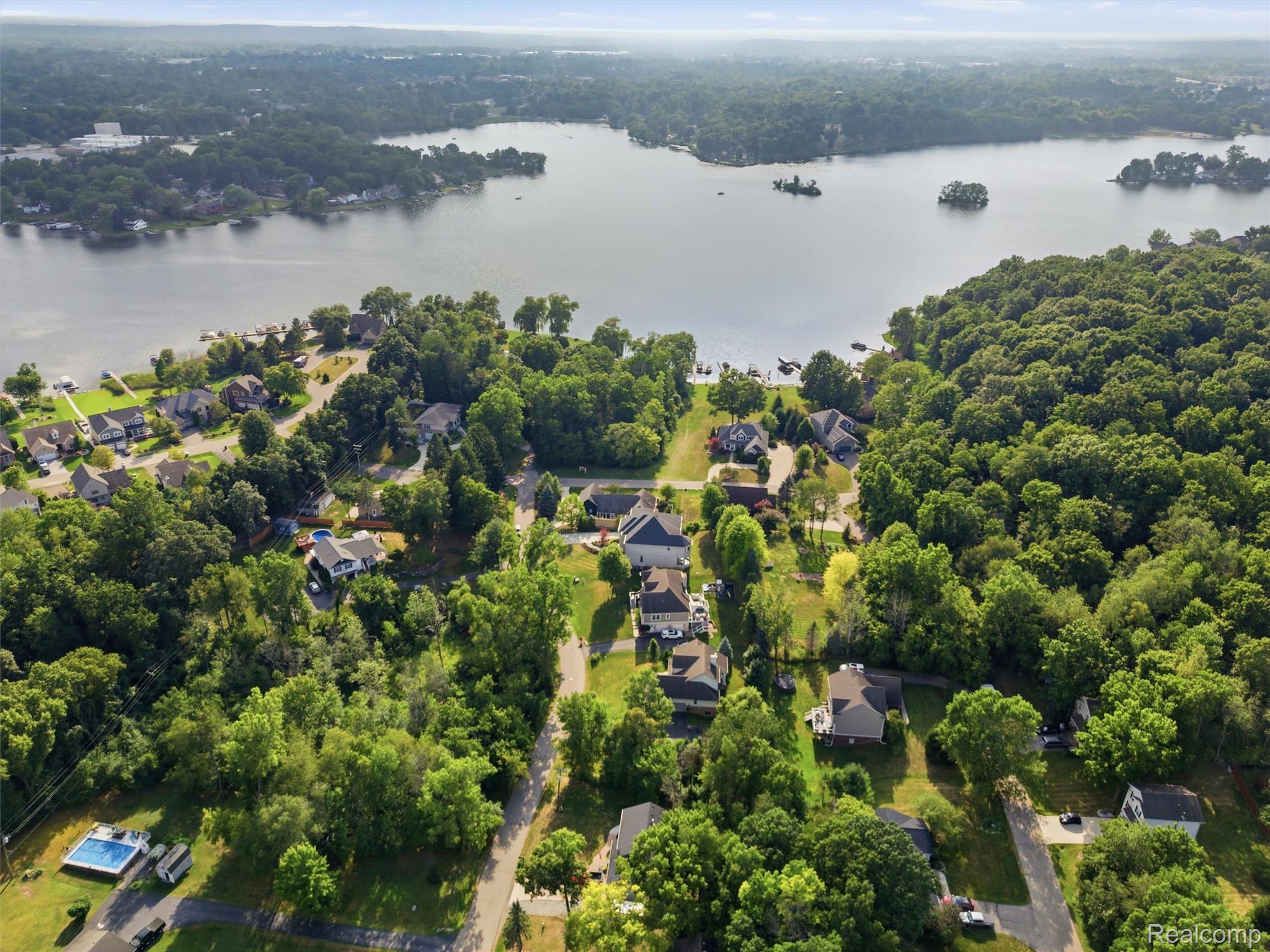 Aerial view of wooded lakeside homes, docks, and a backyard pool.