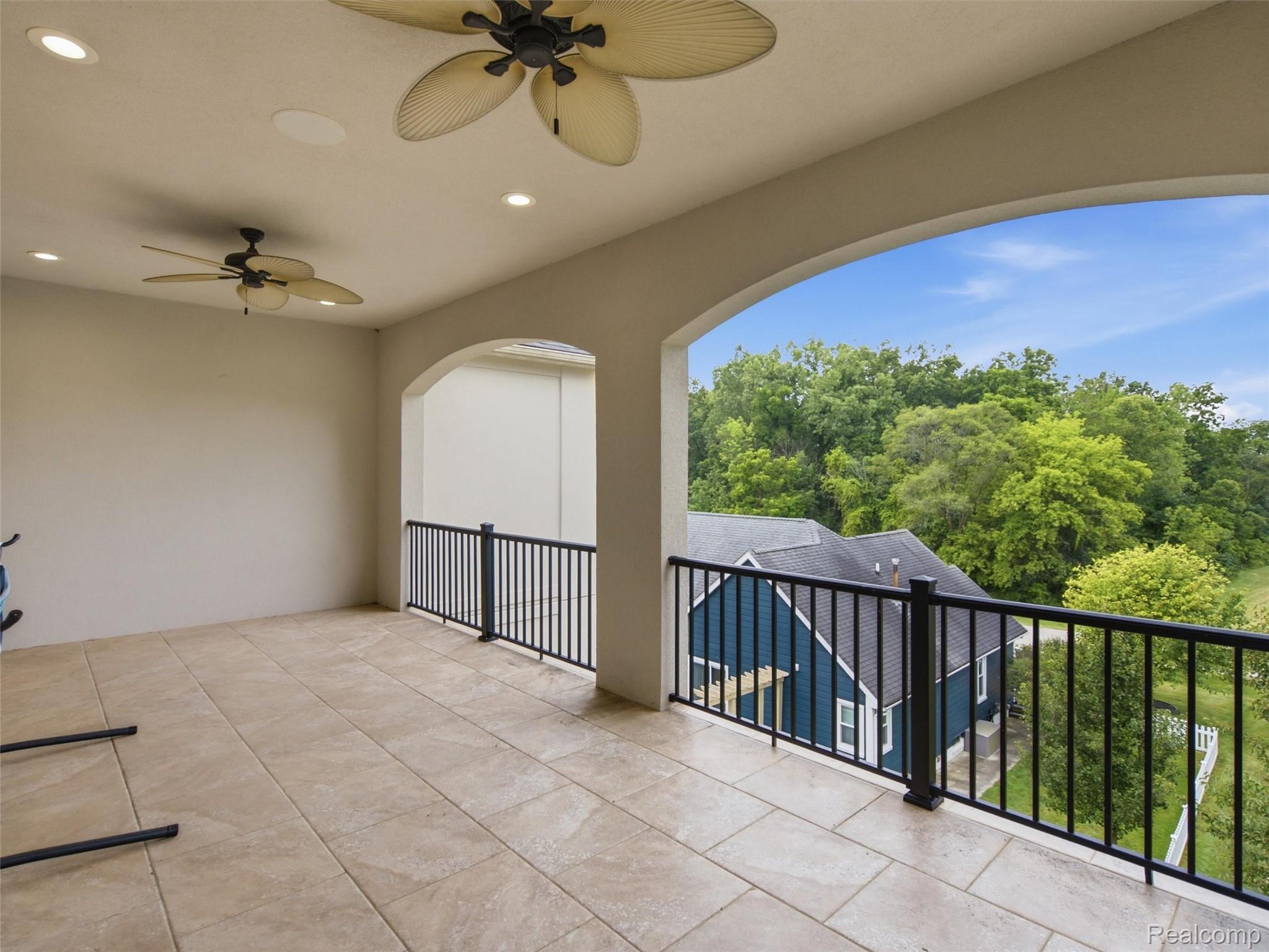 Covered balcony with tiled floor and ceiling fans overlooking trees and a neighboring blue house.