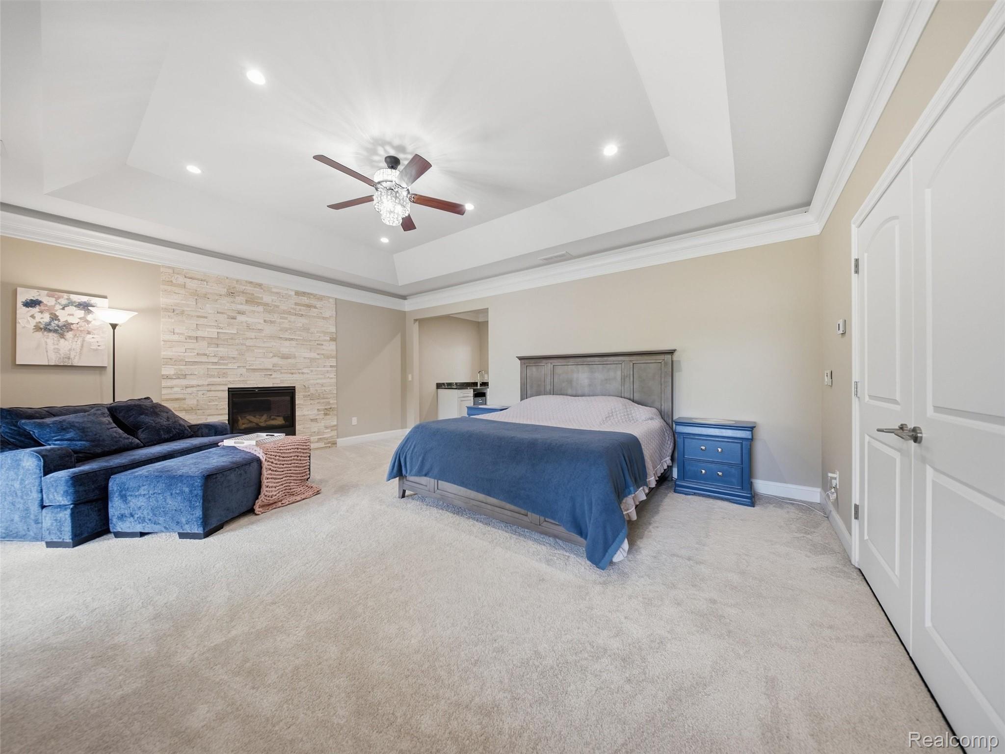 Furnished bedroom with a blue bed and sectional, stone fireplace, and tray ceiling.