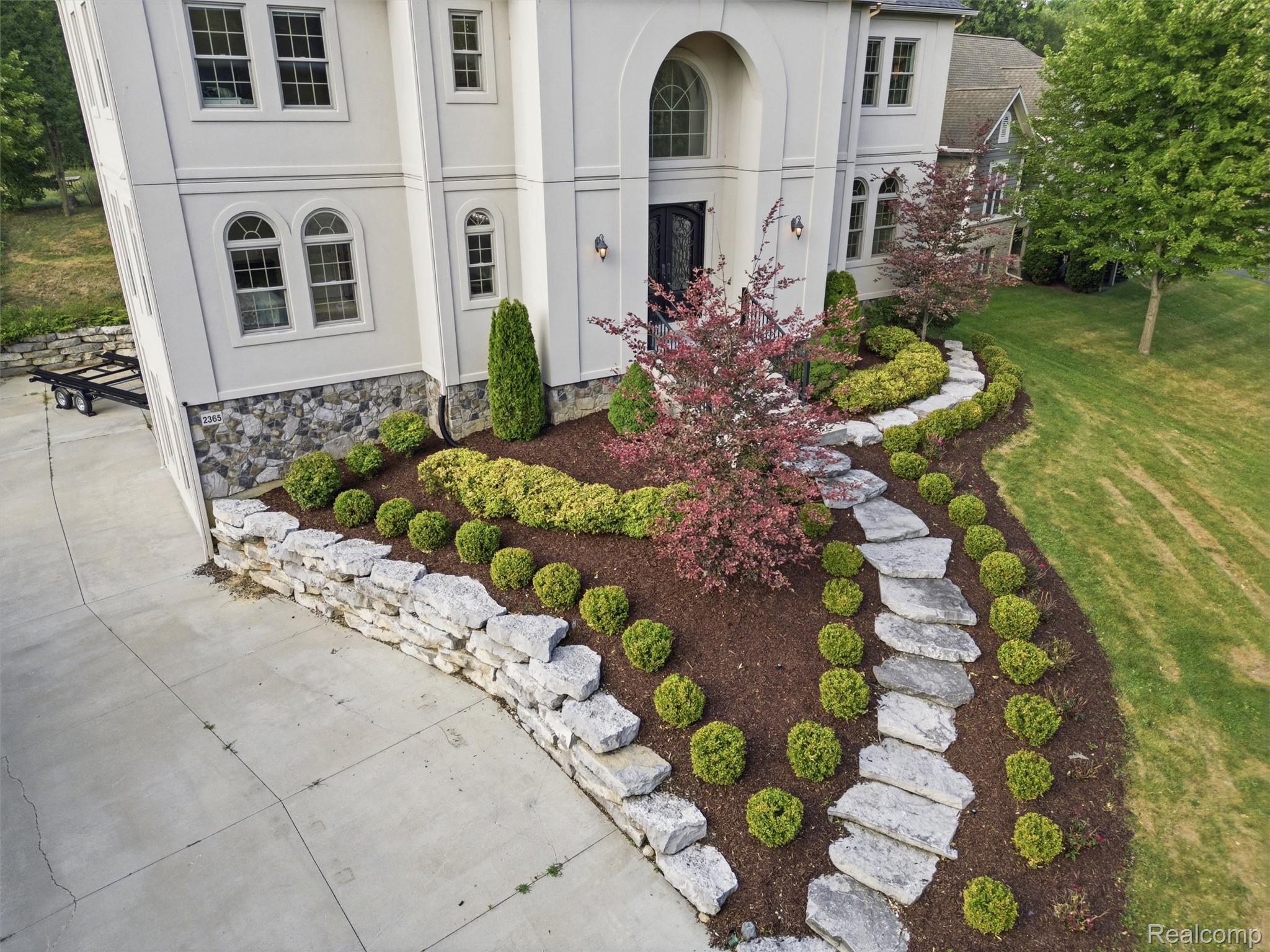 Front of a light-colored house with an arched entry, landscaped garden, and curving stone path.