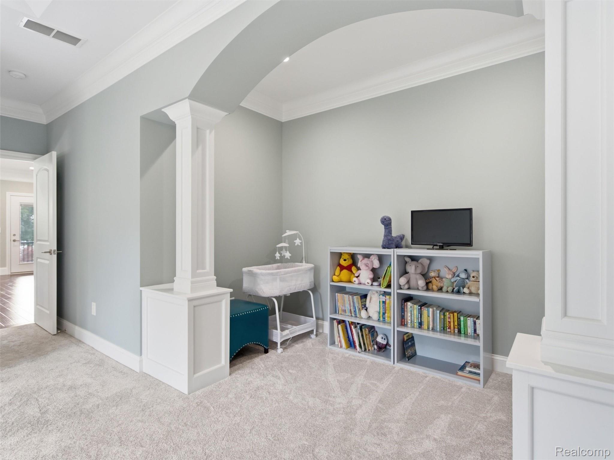 Nursery with a bassinet, toy-filled bookshelves, television, and white columns framing an arched opening.