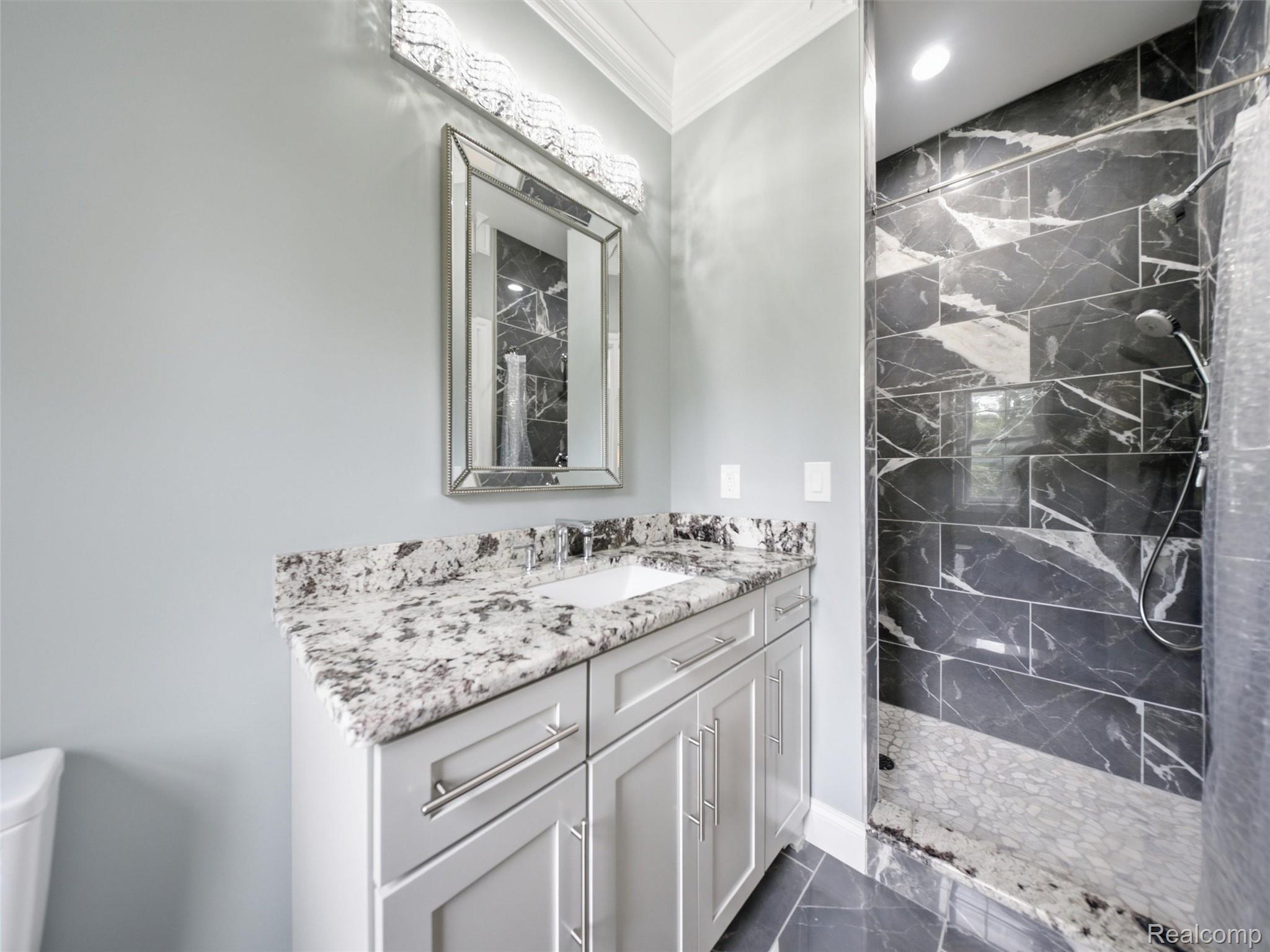 Modern bathroom with a granite-topped vanity and dark marble-look tiled walk-in shower.