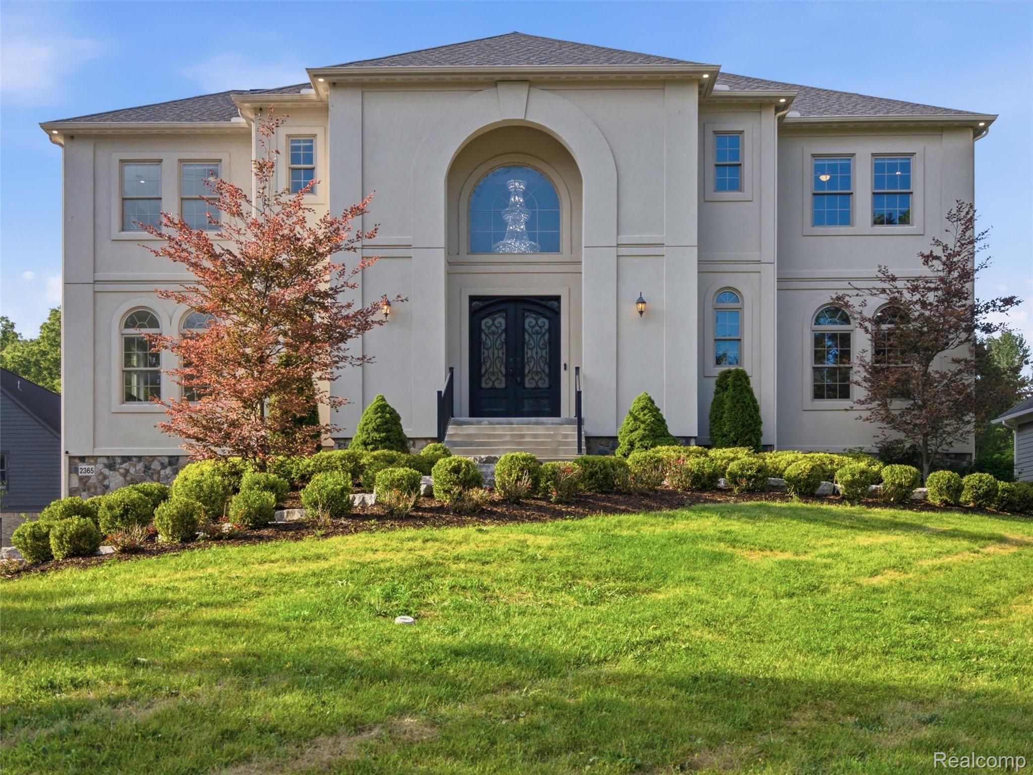 Two-story home with an arched entry, dark double doors, stone accents, and landscaped front lawn.