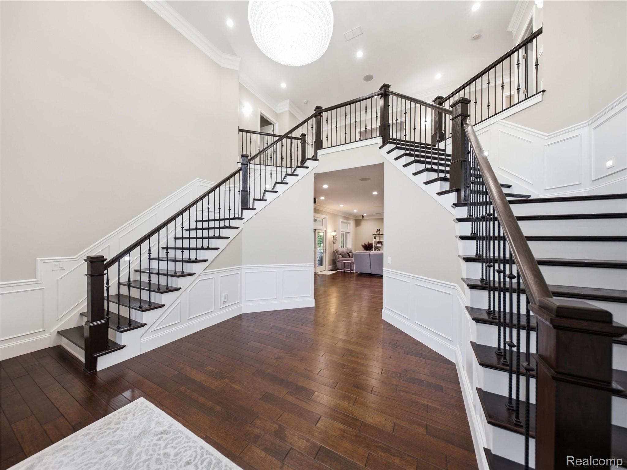 Two-story foyer with twin dark-wood staircases, iron balusters, and white paneled walls.