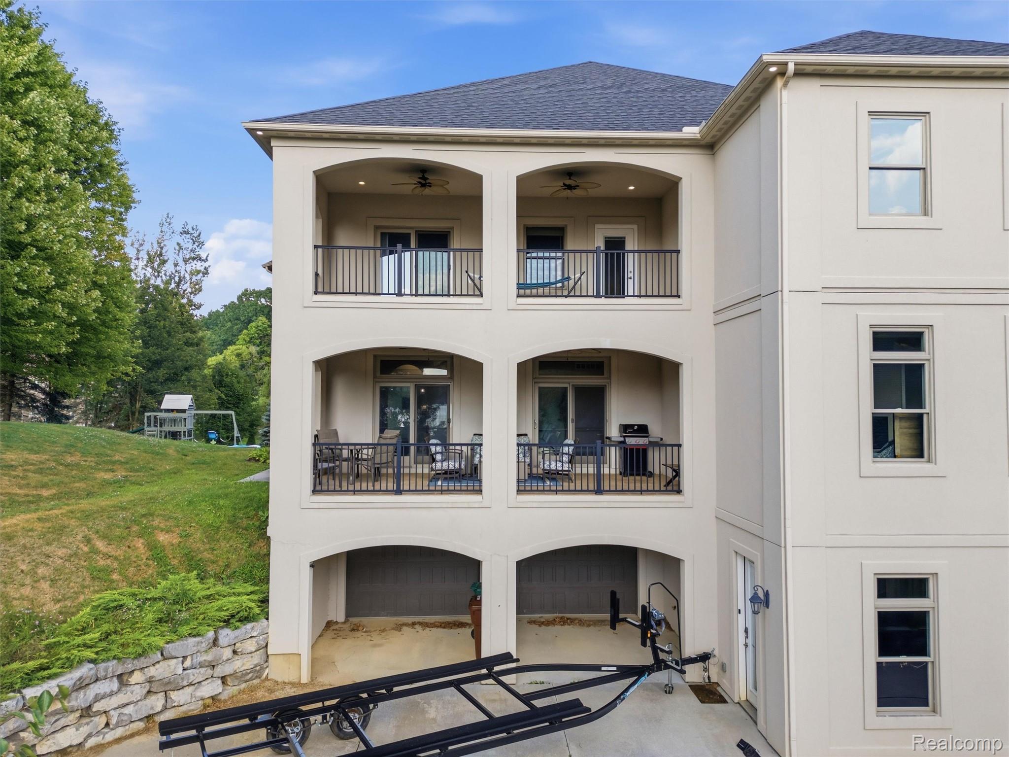 Three-story home with covered balconies, garage bays, and a boat trailer in the driveway.