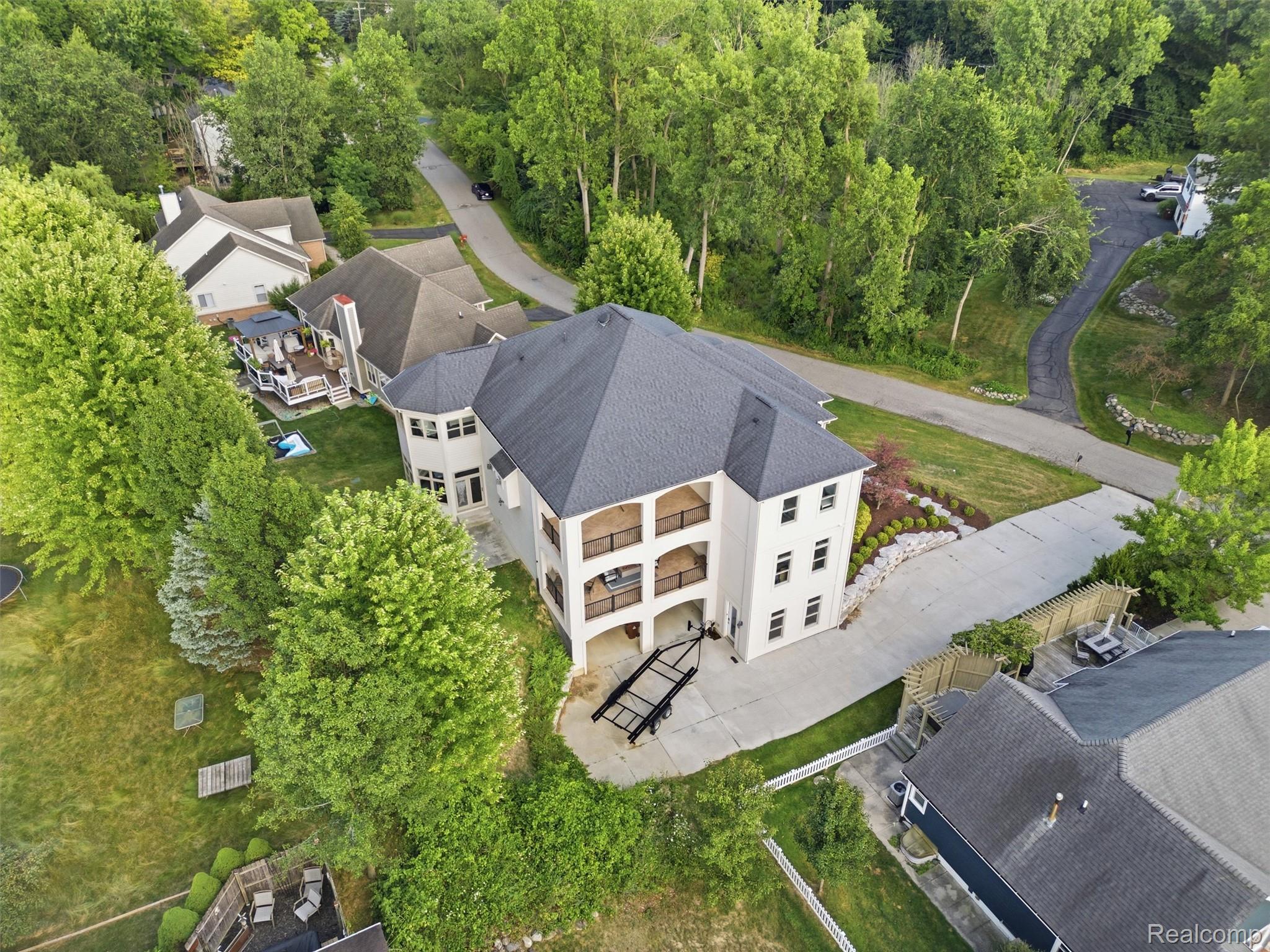 Aerial view of a white multi-story home with balconies, a broad driveway, and mature trees.