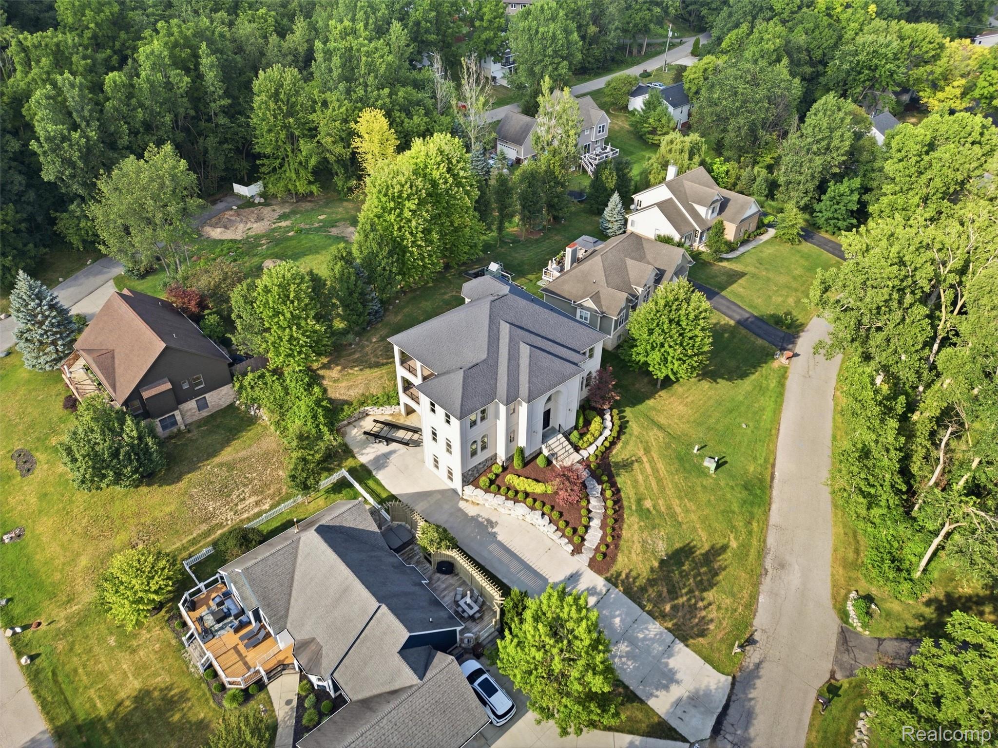 Aerial view of a white multi-story home with a landscaped garden and wooded surroundings.