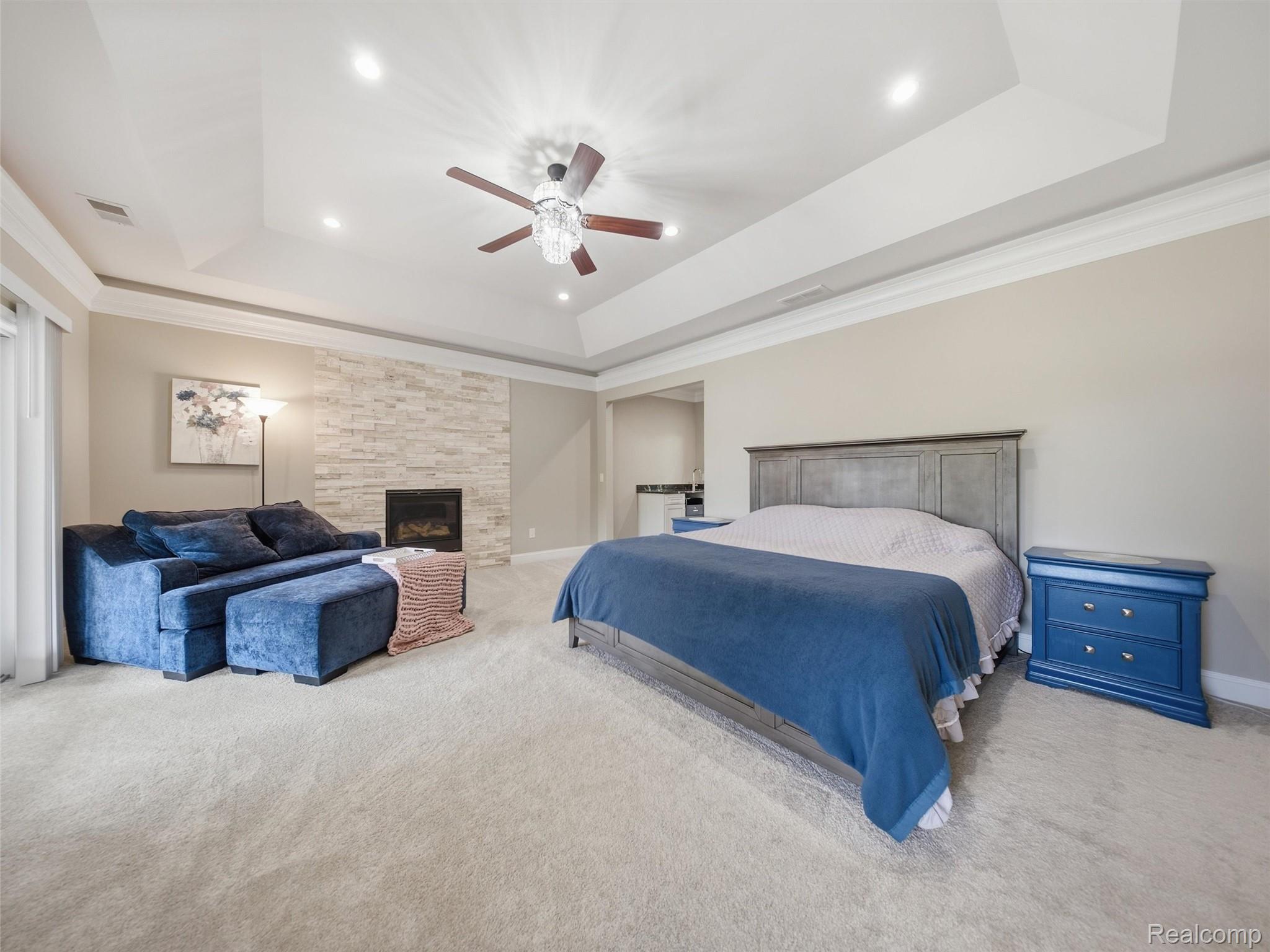 Bedroom with a blue-covered bed, blue sectional sofa, stone fireplace, and tray ceiling.