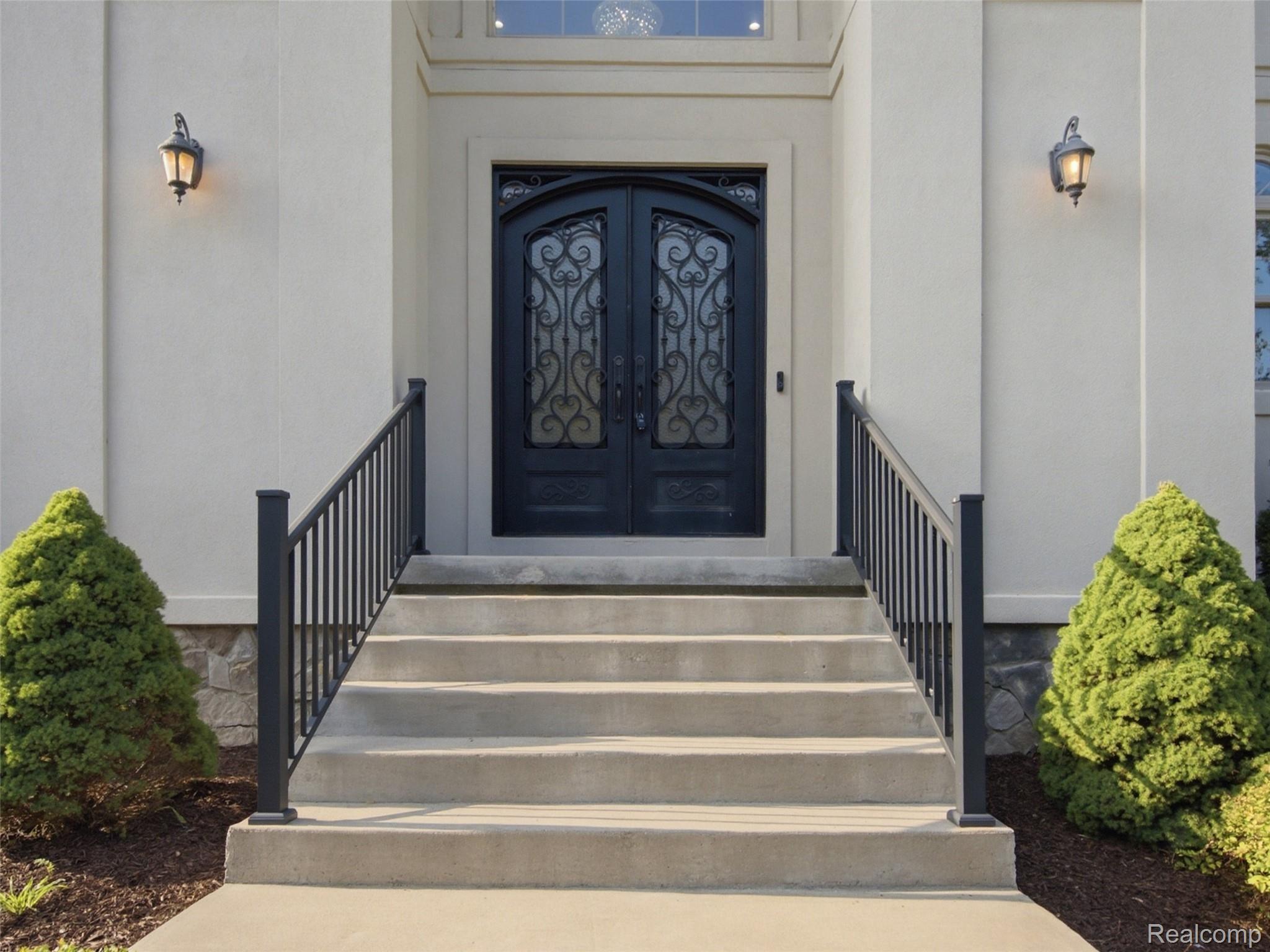Front entrance with concrete steps, black railings, and ornate double doors.