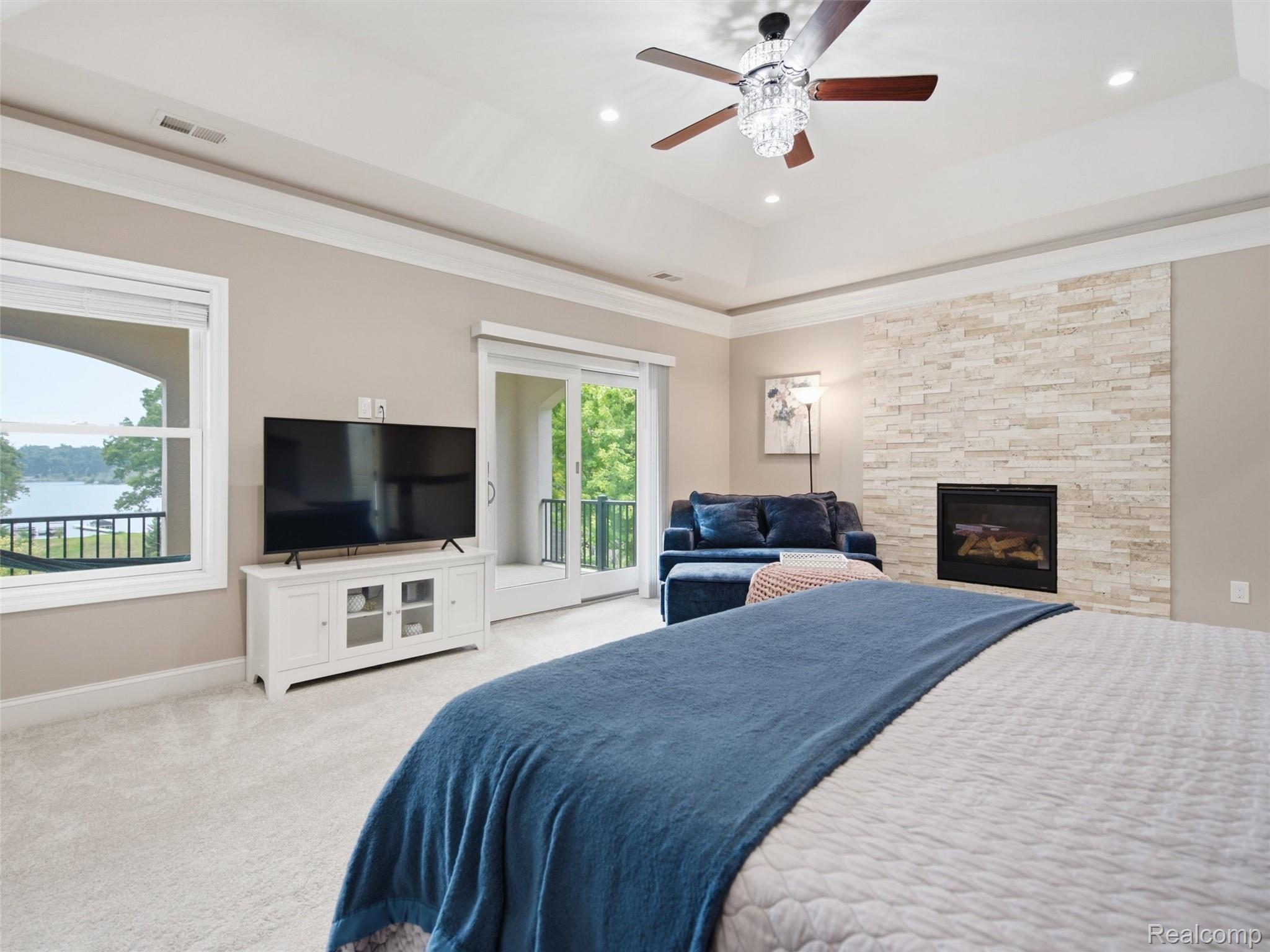 Bedroom with stone fireplace, blue sofa, and lake views through windows and a sliding glass door.