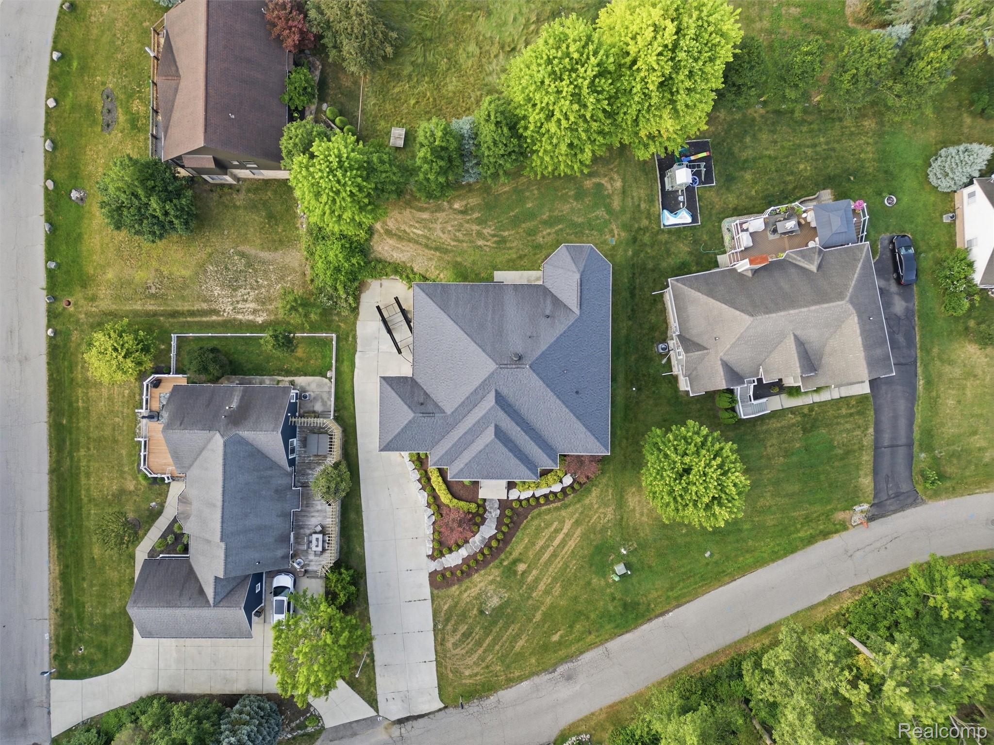 Aerial view of a home with a landscaped front garden, driveway, and surrounding suburban houses.